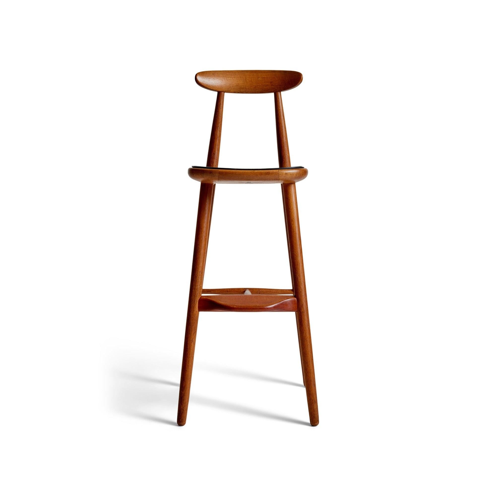 An oak barstool with a black leather seat pad.