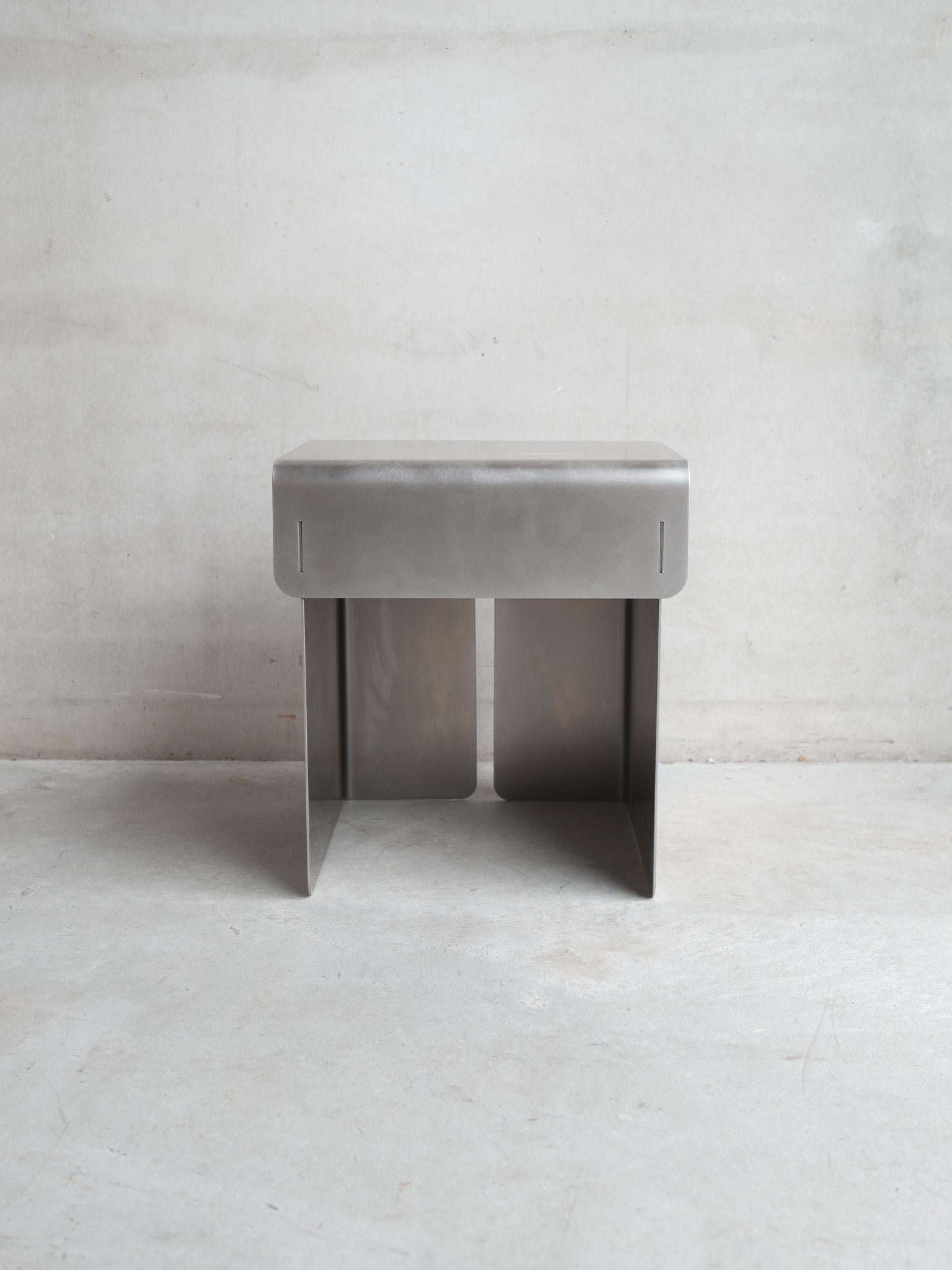 Dieser Hocker aus Edelstahl der belgischen Designerin Rebecca Ackaert destilliert ihre architektonische Designsprache in eine kompakte, skulpturale Form. Mit einer Höhe von 45 cm, einer Breite von 40 cm und einer Tiefe von 35 cm spiegelt das Werk
