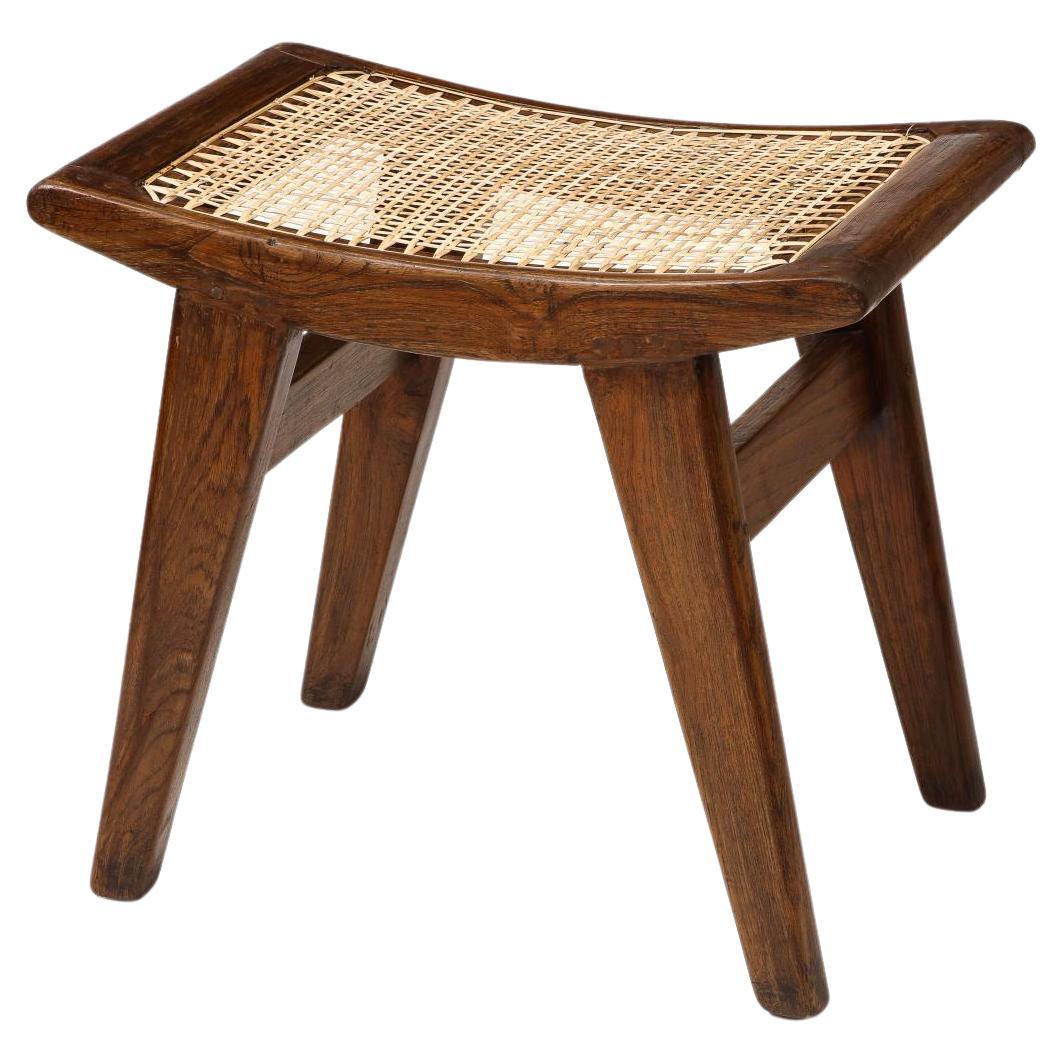 Petite stool with a satisfying visual weight. The tone of the wood is quite warm, with beautiful patina. The seat cushion can be removed to reveal a simply caned seat.