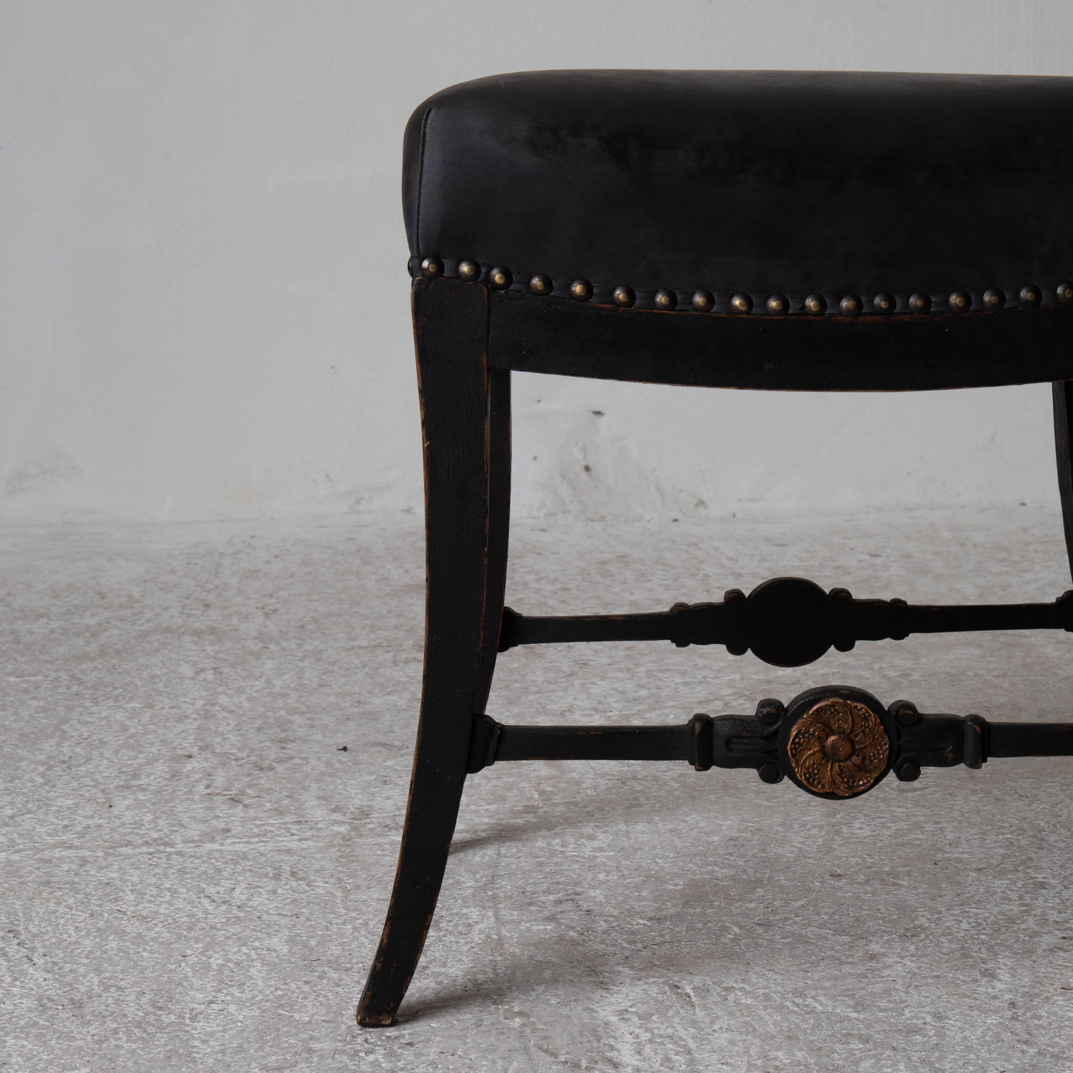 Un tabouret fabriqué pendant la période Karl Johan 1810-1830 en Suède. Refini dans notre Laserow Black. Rembourré dans un cuir noir qui est fini avec des têtes de clous en laiton.