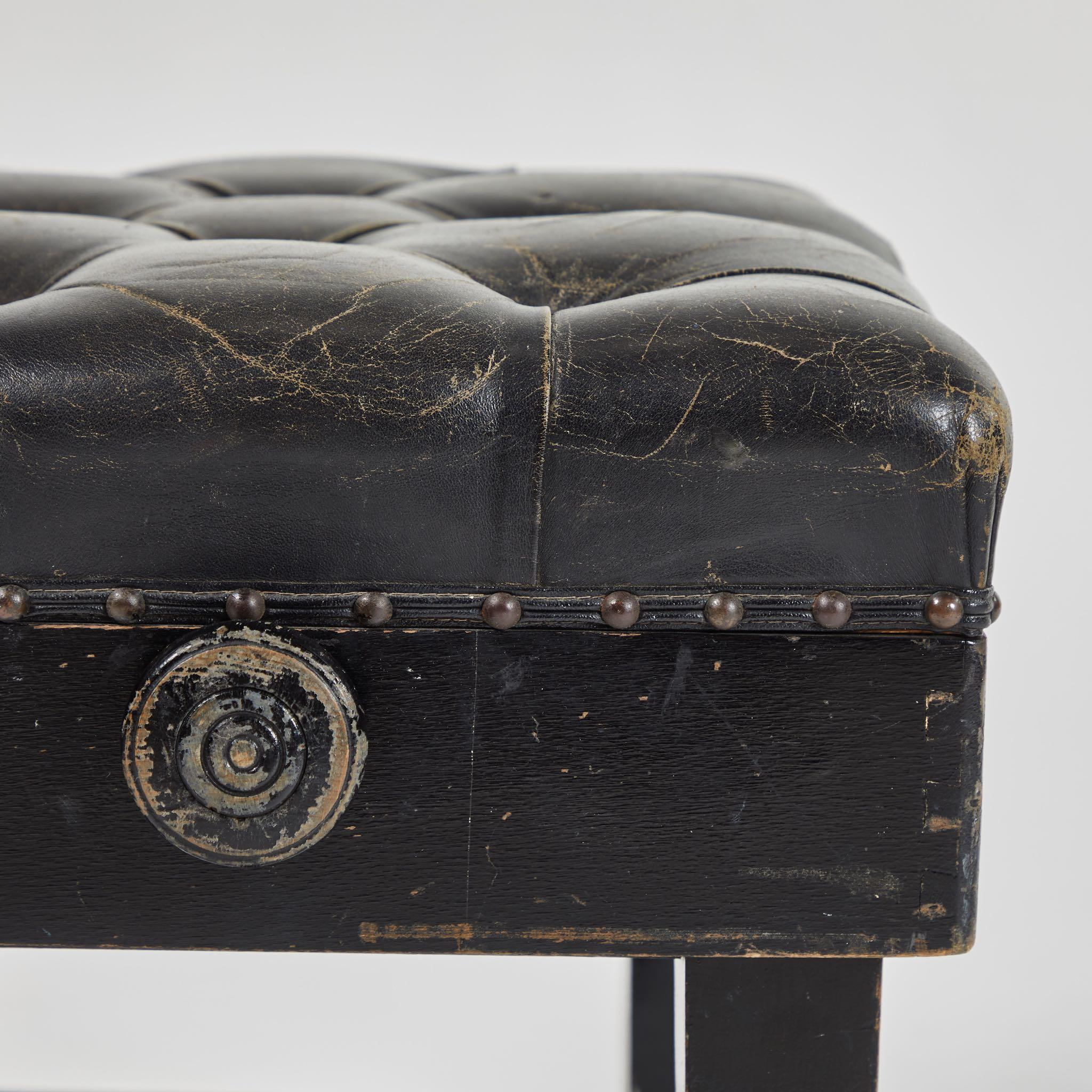 A stool upholstered in black leather, originating in France, circa 1900.