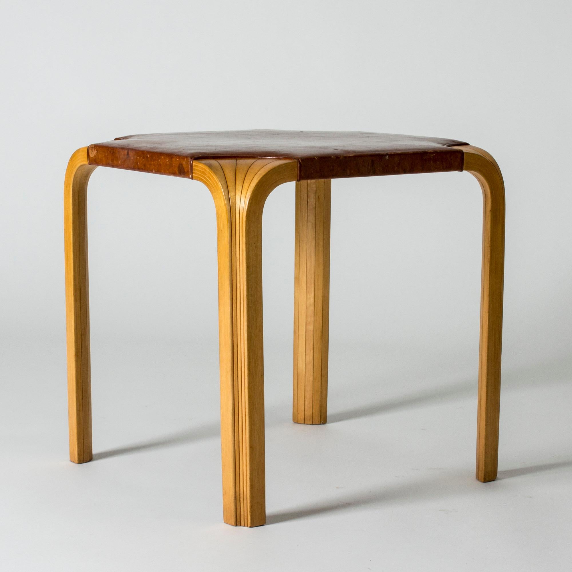 Beautiful stool by Alvar Aalto, model X601, featuring the signature fan design on the legs. Very nicely patinated original, brown leather seat.