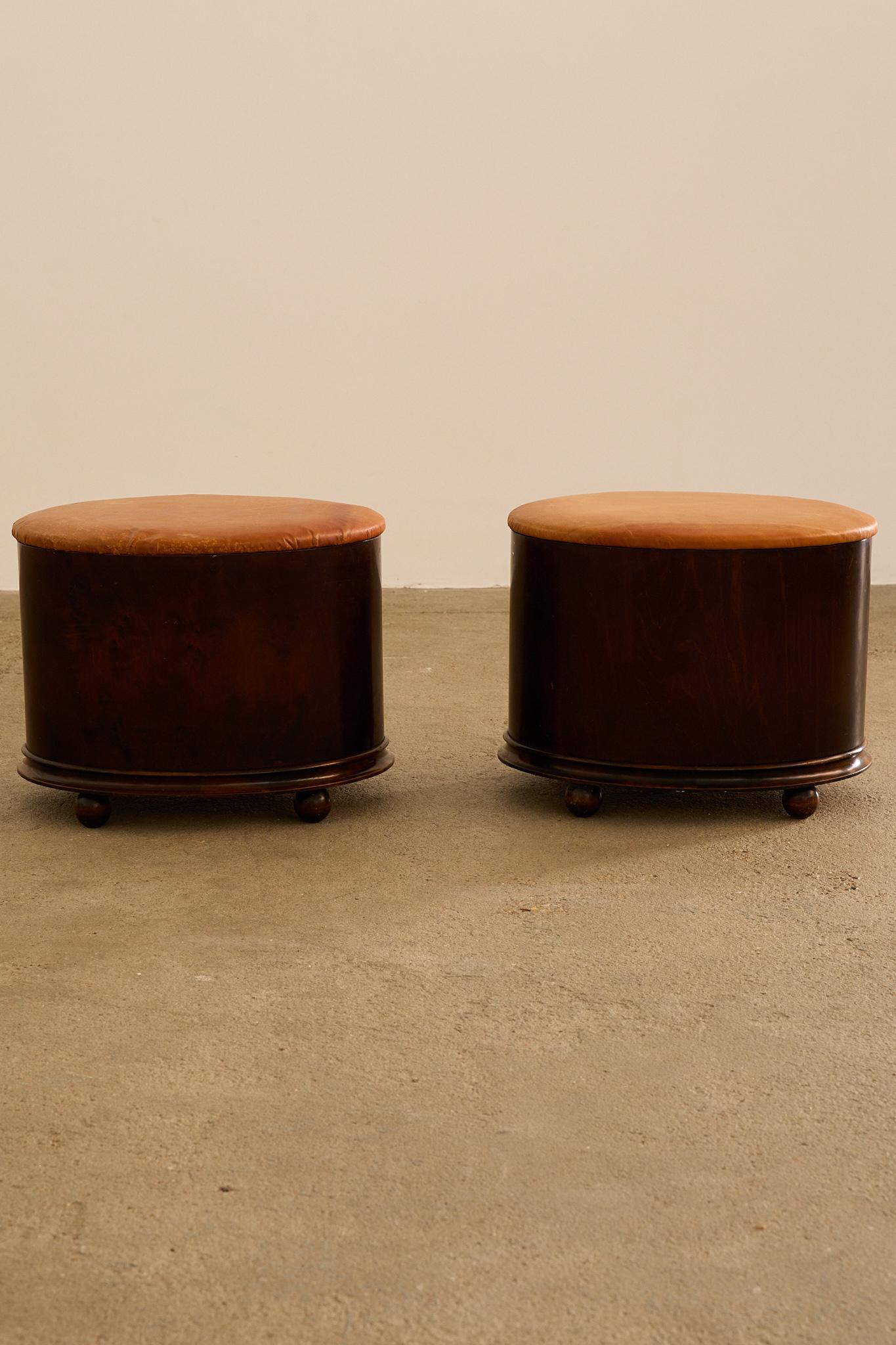 Paire de poufs ovales à couvercle des années 1940, fabriqués en placage d'acajou à l'extérieur et en pin à l'intérieur. Chacune repose sur une plinthe en bois de noyer avec de petits pieds boules, et les couvercles à charnière sont recouverts de