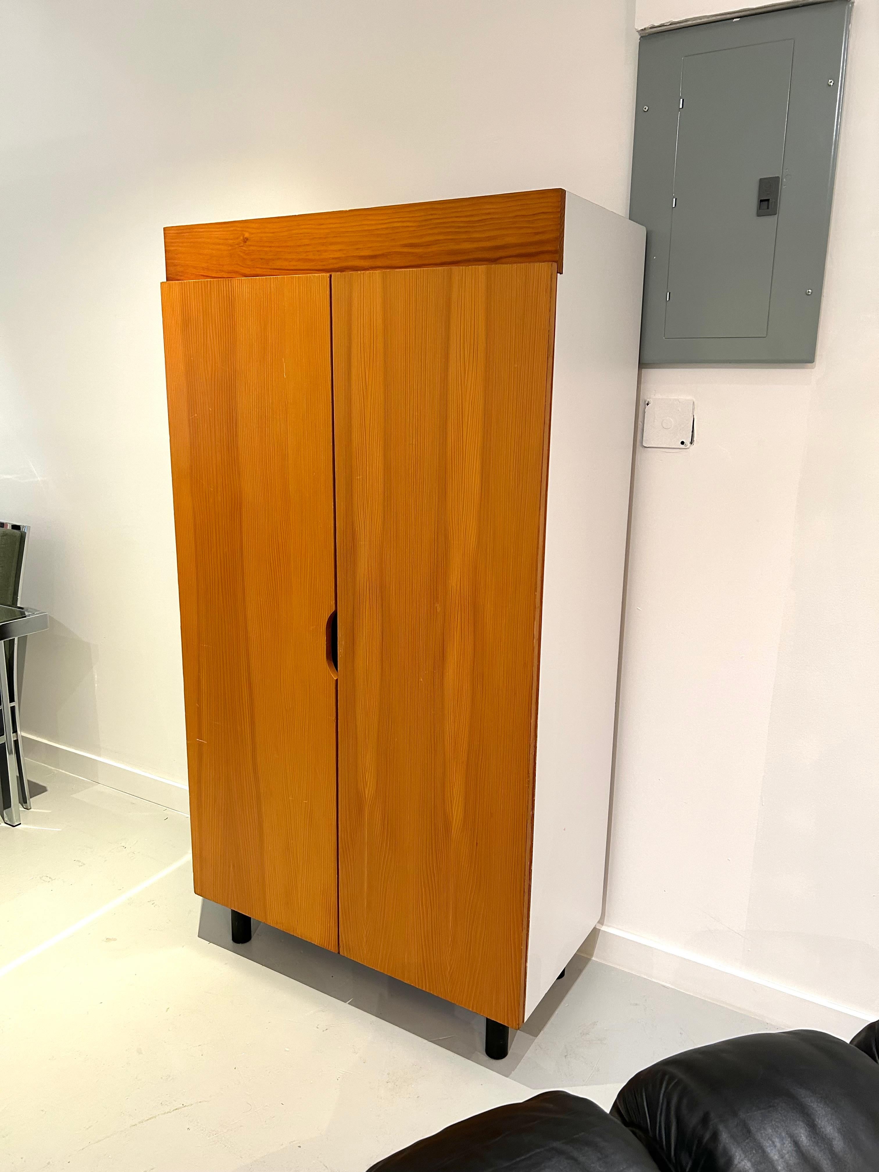 Two door wardrobe/storage cabinet designed by Charlotte Perriand in the 1960s for Les Arcs Ski Resort in Savoie, France (the French Alps), made in pinewood, pine veneer, and white laminate. The cabinet is supported on four cylindrical, black