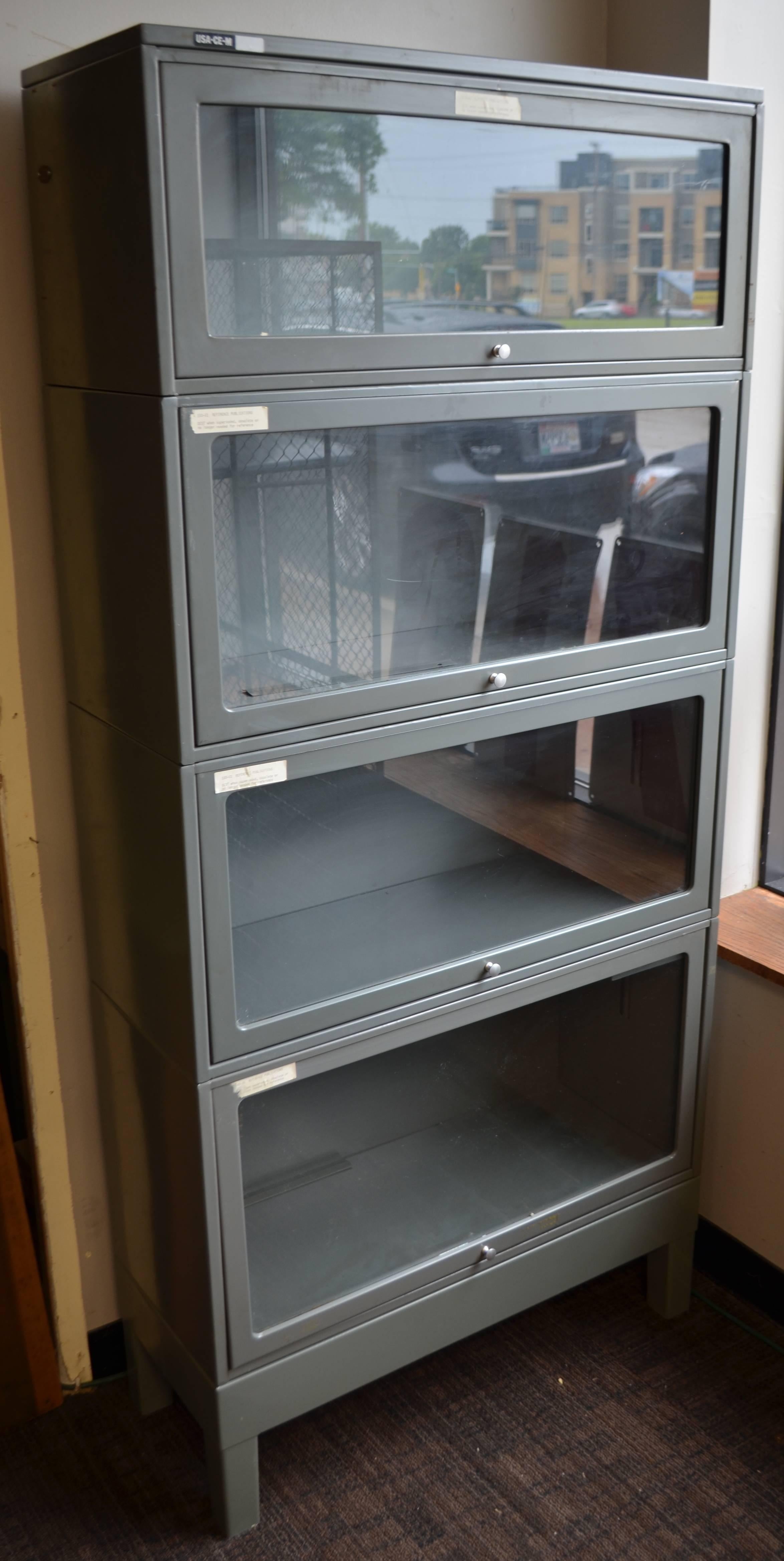 Storage file cabinet from lawyer's barrister. Painted steel with four shelves behind glass door fronts that slide up and in to open. Excellent working order. Ideal way to store and protect behind glass dishware, glassware, memorabilia, books,