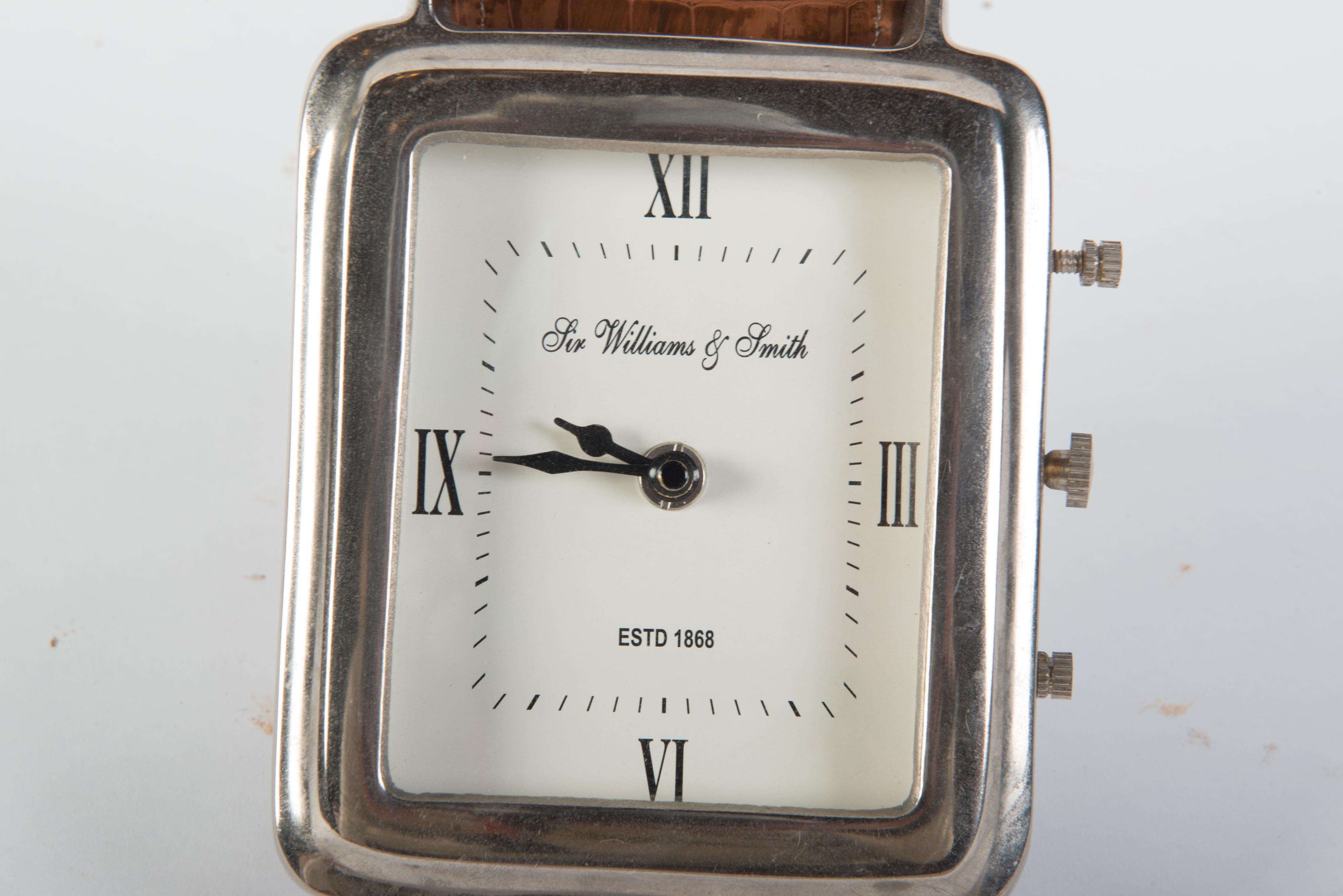 Horloge de bureau avec montre-bracelet de présentation du magasin Sir Williams & Smith, avec bracelets en cuir. Le cadran de l'horloge mesure 5 pouces sur 6 pouces de haut. Une petite pièce en métal permet de relever la montre à un angle. Fonctionne