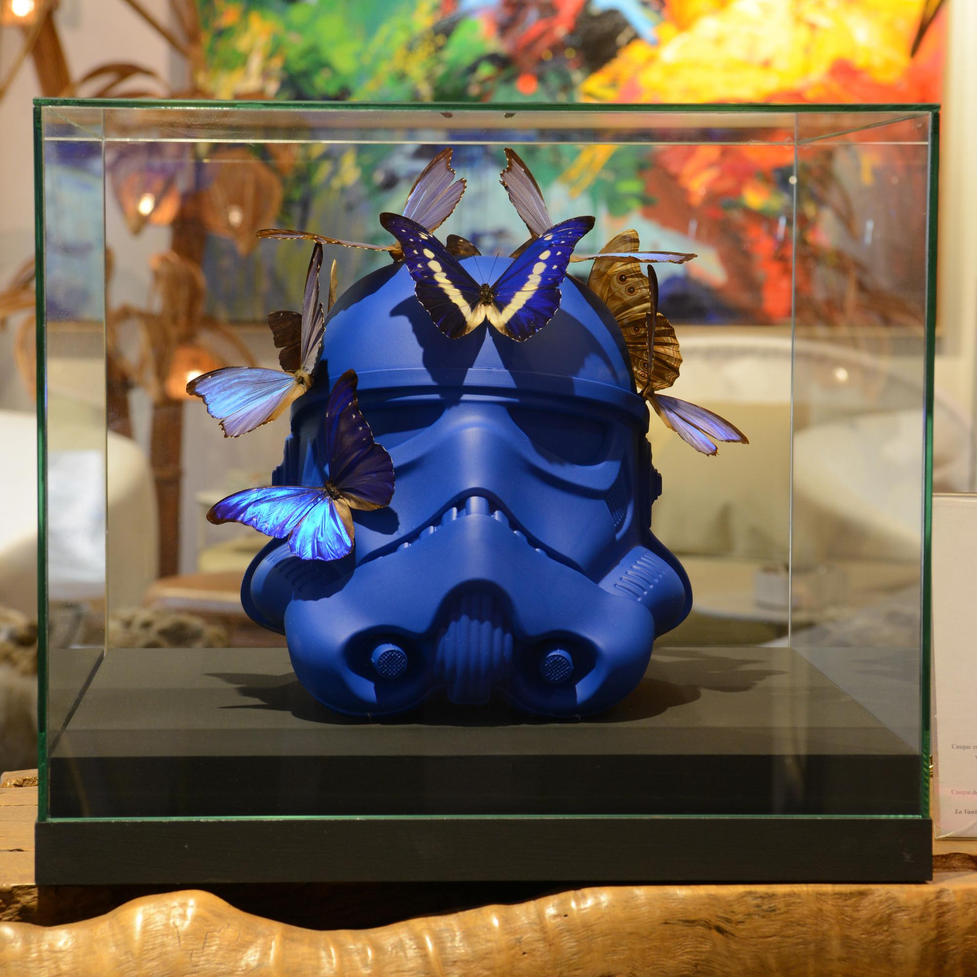 Sculpture Stormtrooper Bleu Casque Papillons avec original
Casque Stormtrooper bleu en résine bleue mate ornementée
avec les papillons Morphos (aucune citation n'est nécessaire pour ce papillon). 
Vitrine en verre anti-reflet Securit avec base en