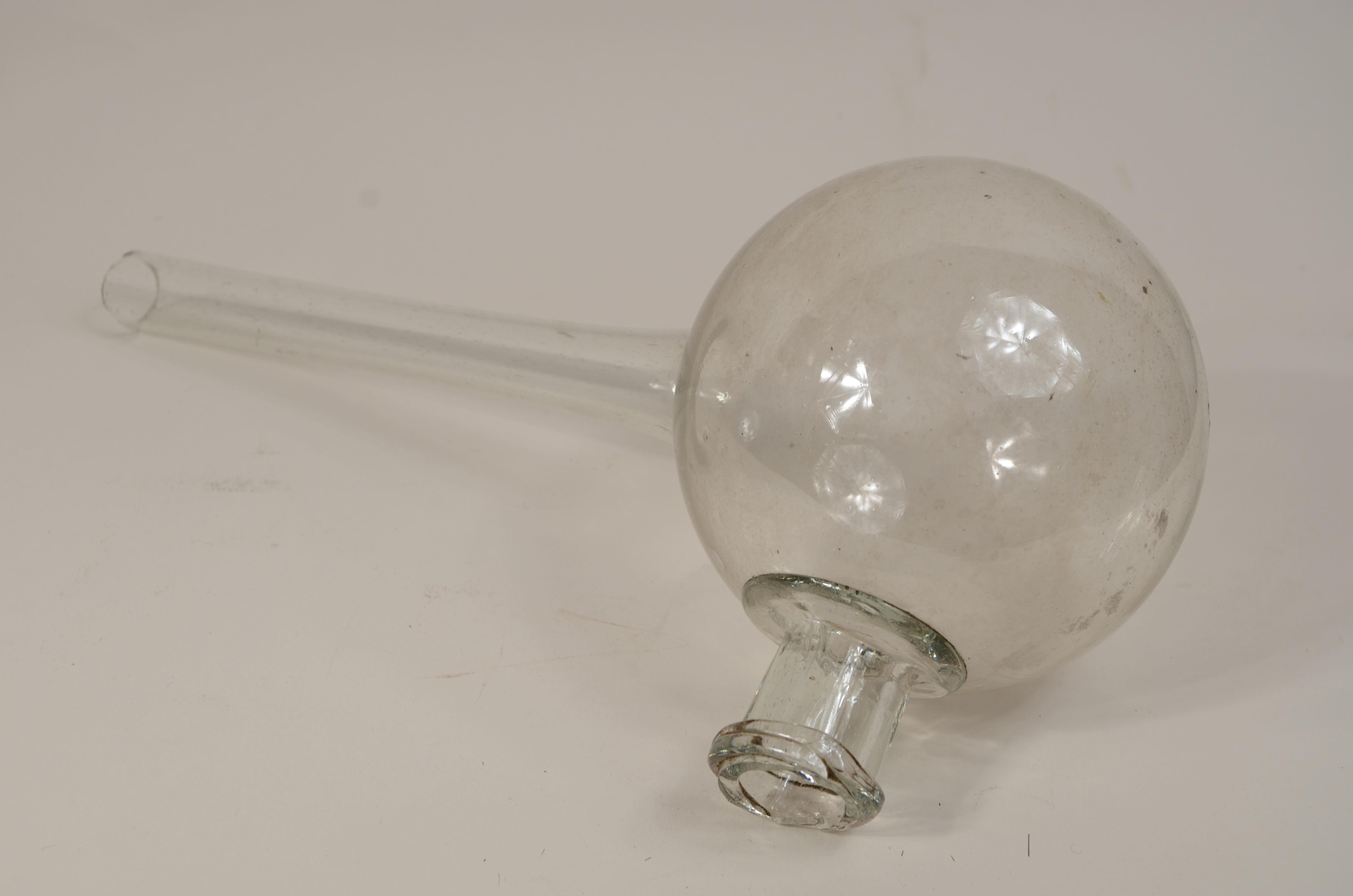 Transparent blown glass laboratory retort from the early 19th century, used for distillation, has a spherical body and long neck in the center. 
Very Good Condition. Measures length cm 30 - inch 11.8, height cm 14 -inch 5.5, width cm 11 - inch 4.3. 