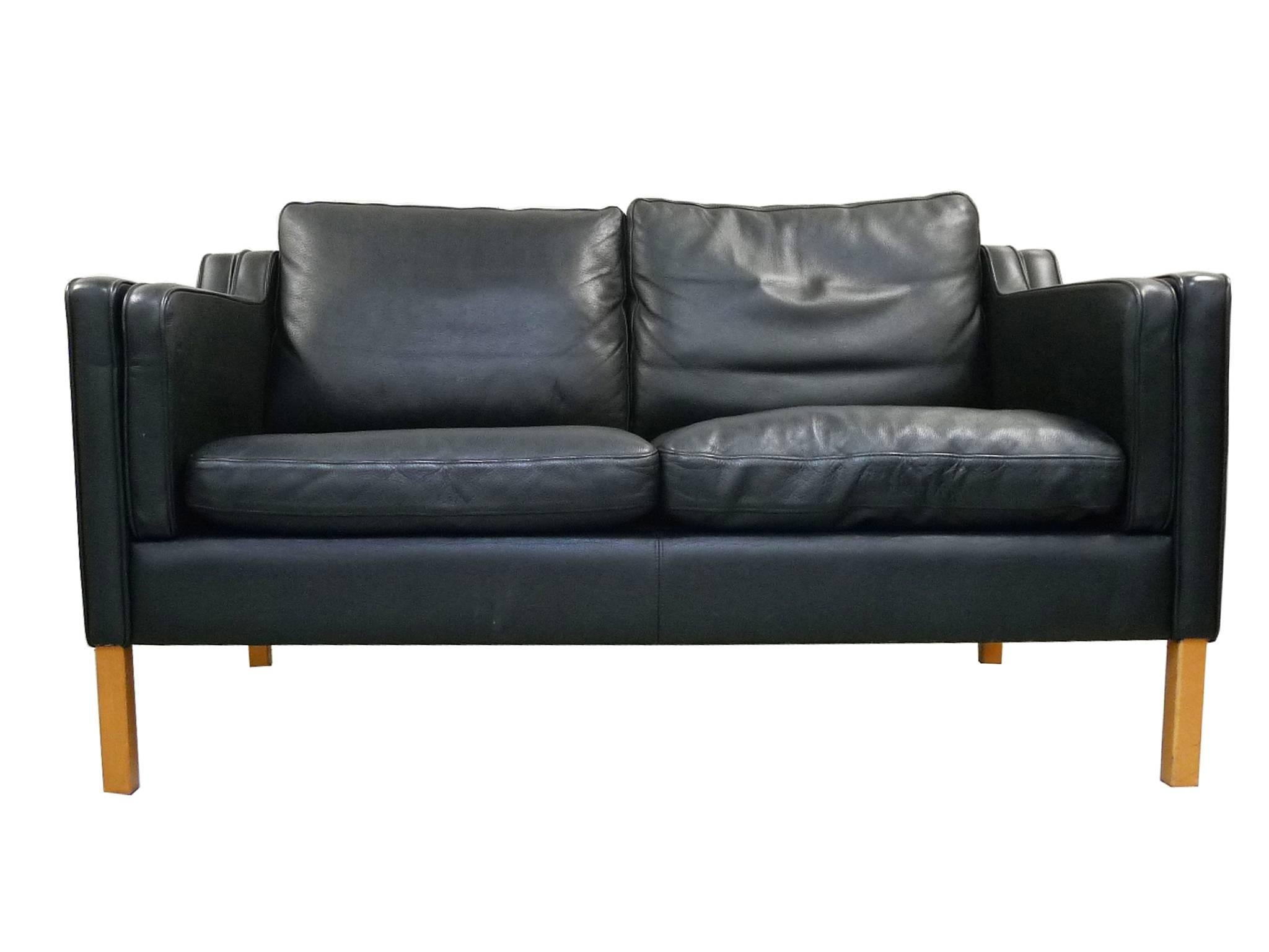 These three settees are in the style of Børge Mogensen and were manufactured by Stouby. Their design is one of clean lines and soft, rounded edges. The upholstery is a well-aged black leather, while the frame is beech wood. These settees have a low