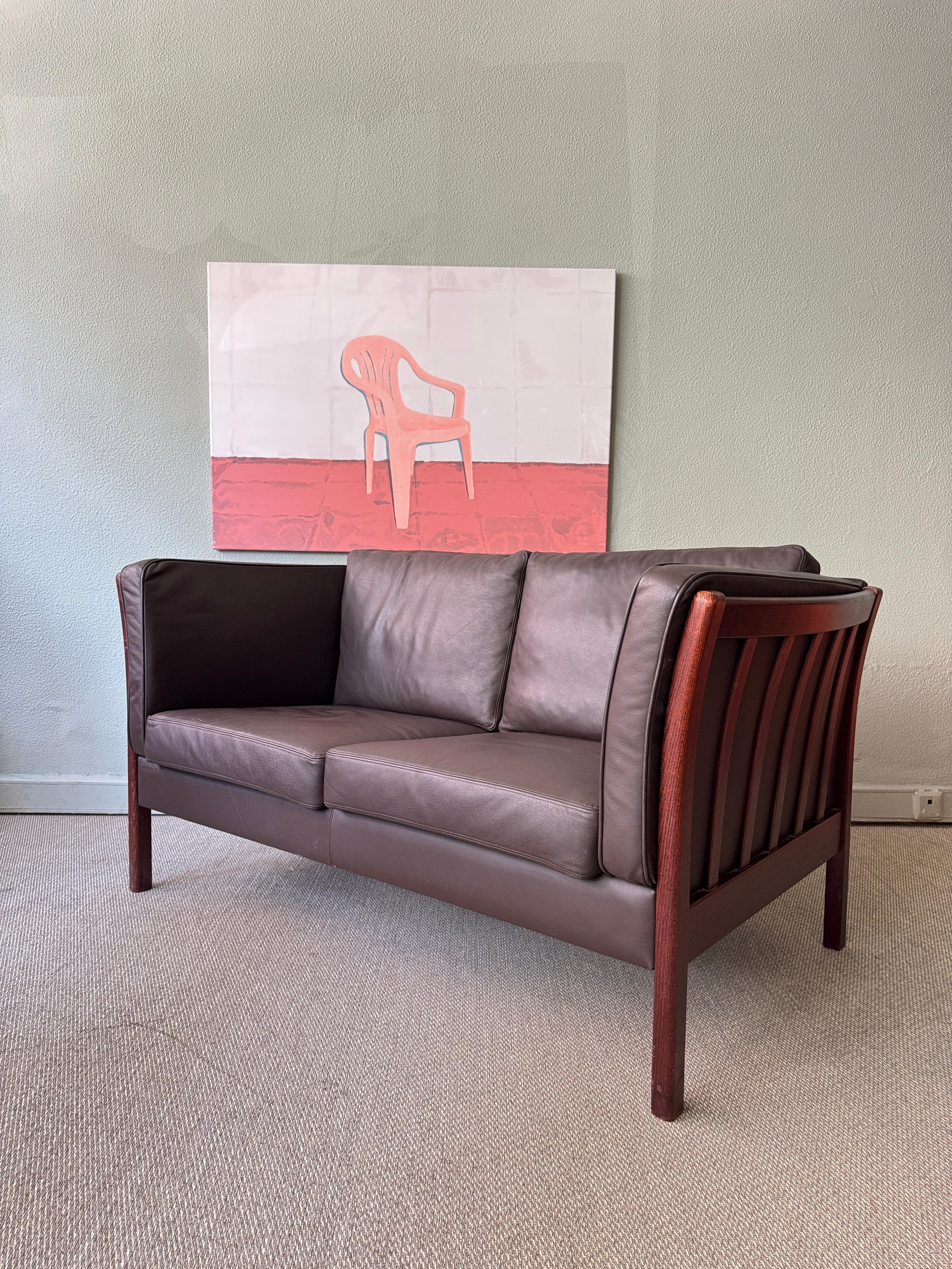 Dänisches Zweisitzer-Sofa von Stouby, hergestellt in den 1980er Jahren. Dieses kompakte, aber optisch beeindruckende Möbelstück ist ein echtes Original, das mit schokoladenbraunem Leder gepolstert ist und dessen massiver Buchenholzrahmen in einem