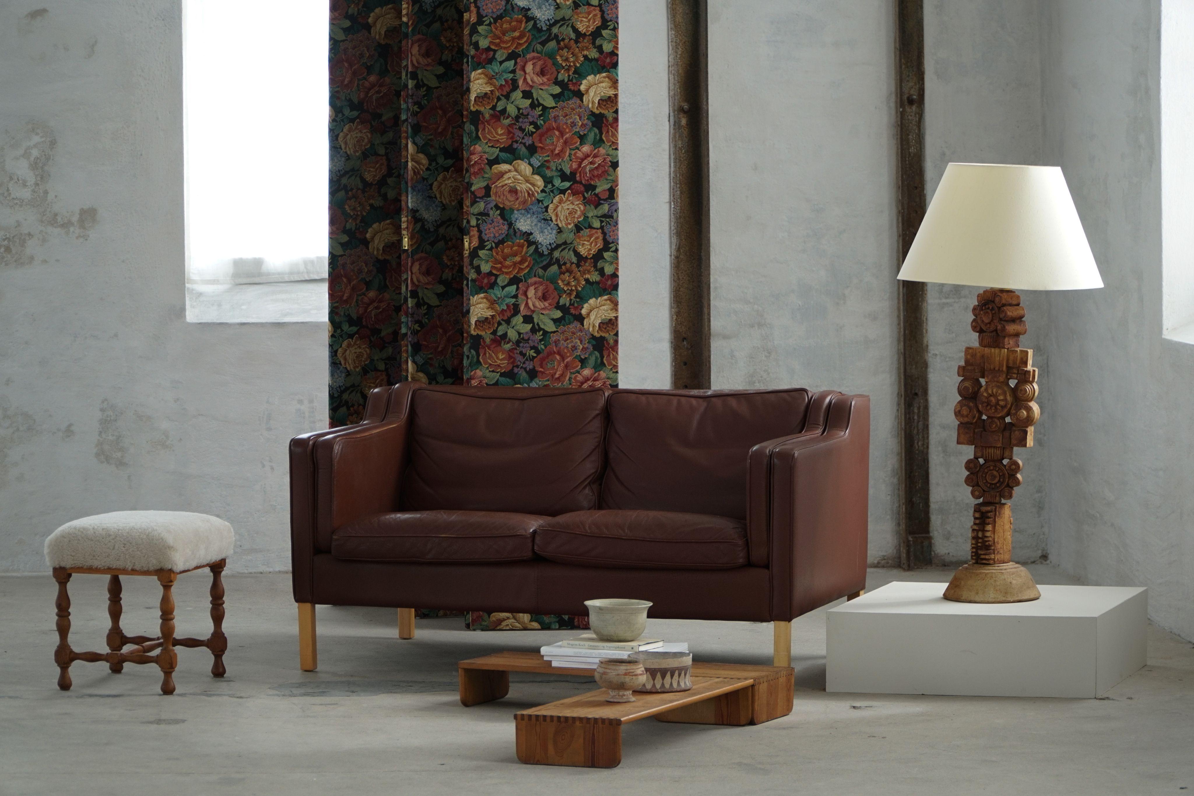 A classic Danish Modern two-seater sofa upholstered in brown leather, resting on legs made from solid beech. With its clean lines, balanced proportions, and timeless comfort, the piece embodies the quiet elegance of 1970s Scandinavian