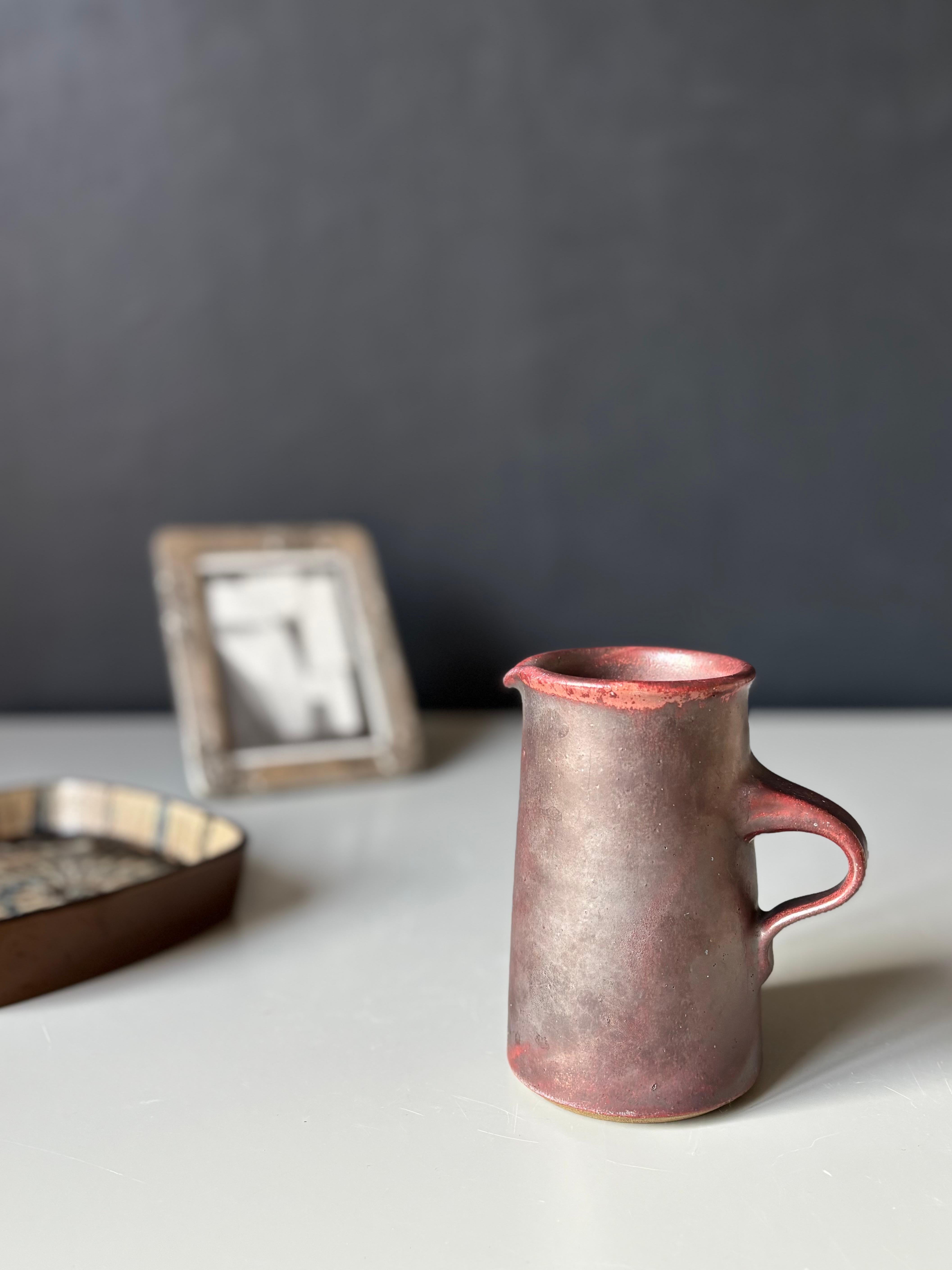 Beautifully glazed dark earthy brown, warm burgundy and fiery red Danish midcentury modern stoneware pitcher designed and handmade by Nis Stougaard on the Danish island of Bornholm in the 1960s. To be used as serveware or a decorative vase. Stamped