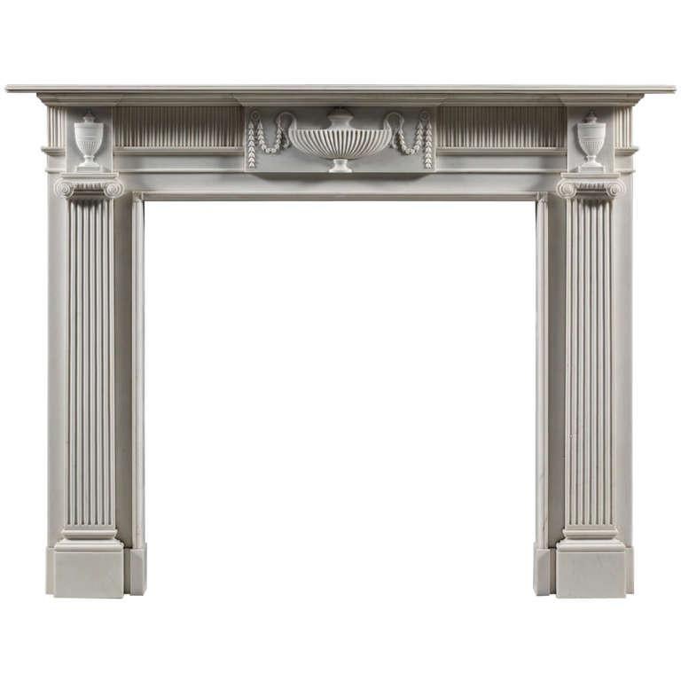 This Irish chimneypiece of the Greek ionic order features a central tablet carved with a ribbed classical tazza shaped vase draped with swags of flowers, housed in a fluted frieze. The corner blocks are adorned with lidded urns and sit above jambs
