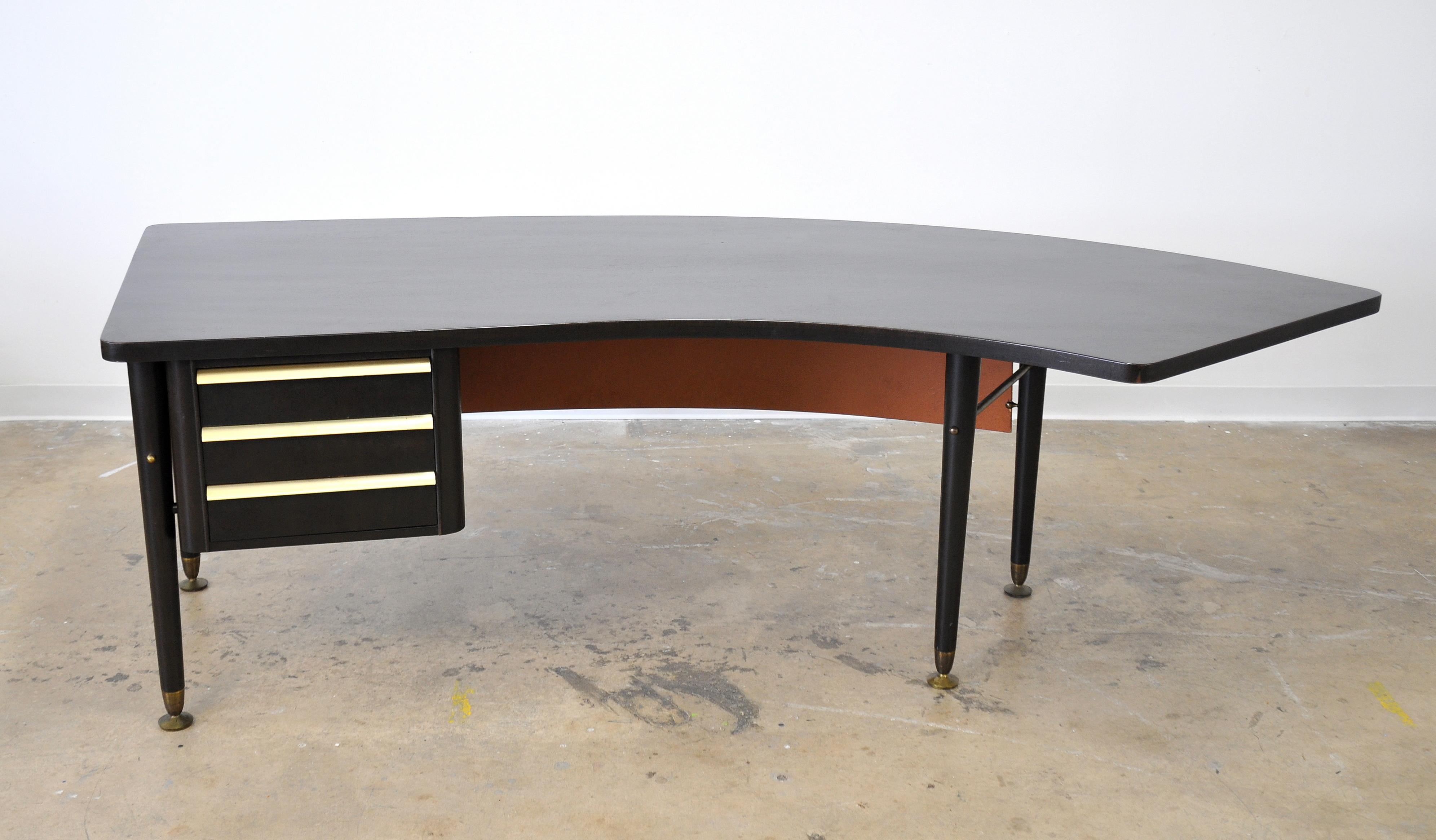Midcentury modern black executive desk, from the Sigma series, manufactured by Stow & Davis in the late 1950s-early 1960s. The writing table features a boomerang shaped top, three drawers with restored brass hardware, a peach colored modesty panel,