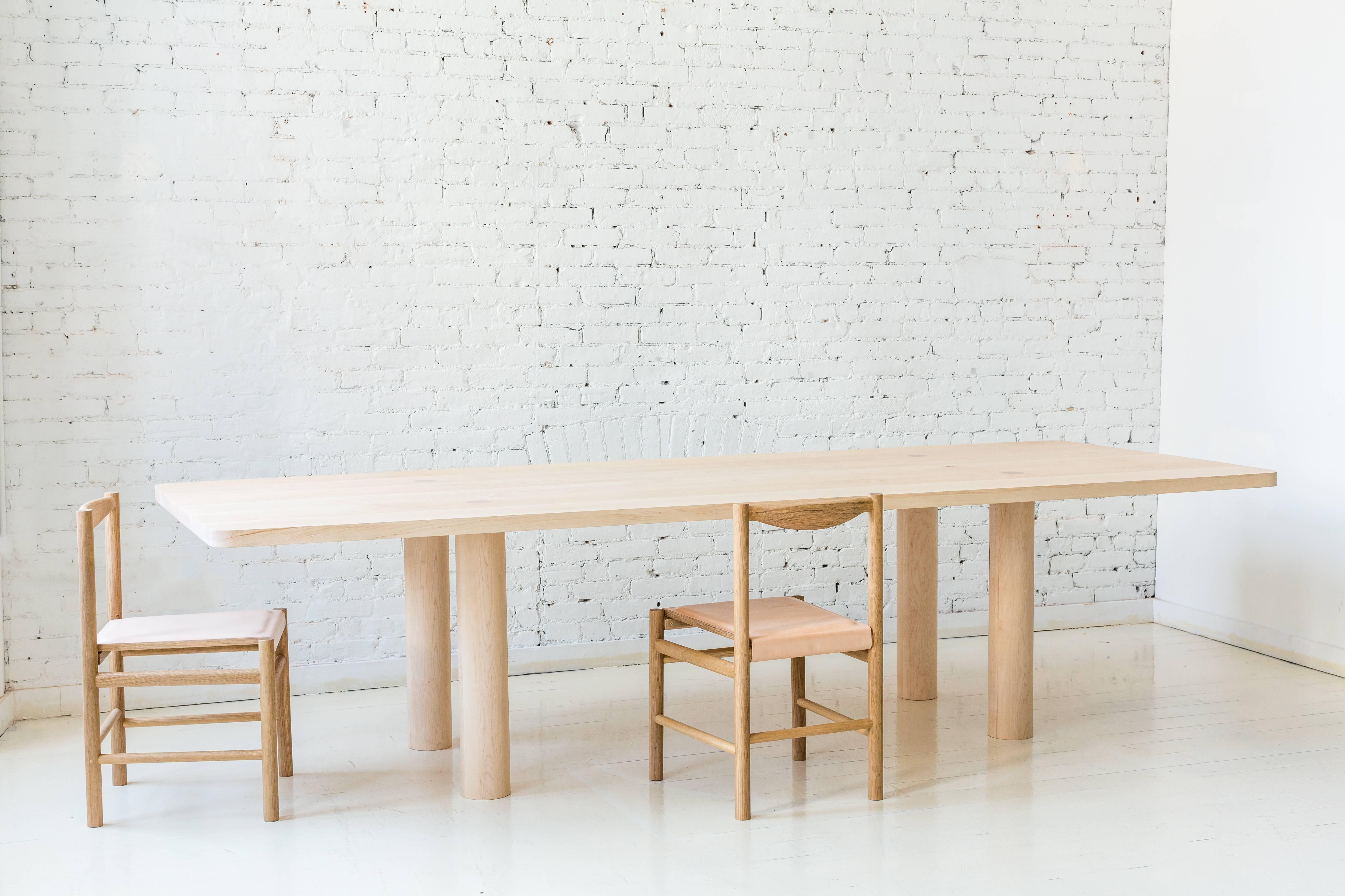 This contemporary, minimal dining table features a two inch thick hardwood top and four large round legs with no other structural base components. Each leg has a tenon that pierces the top, revealing the joinery. This subtle, important detail