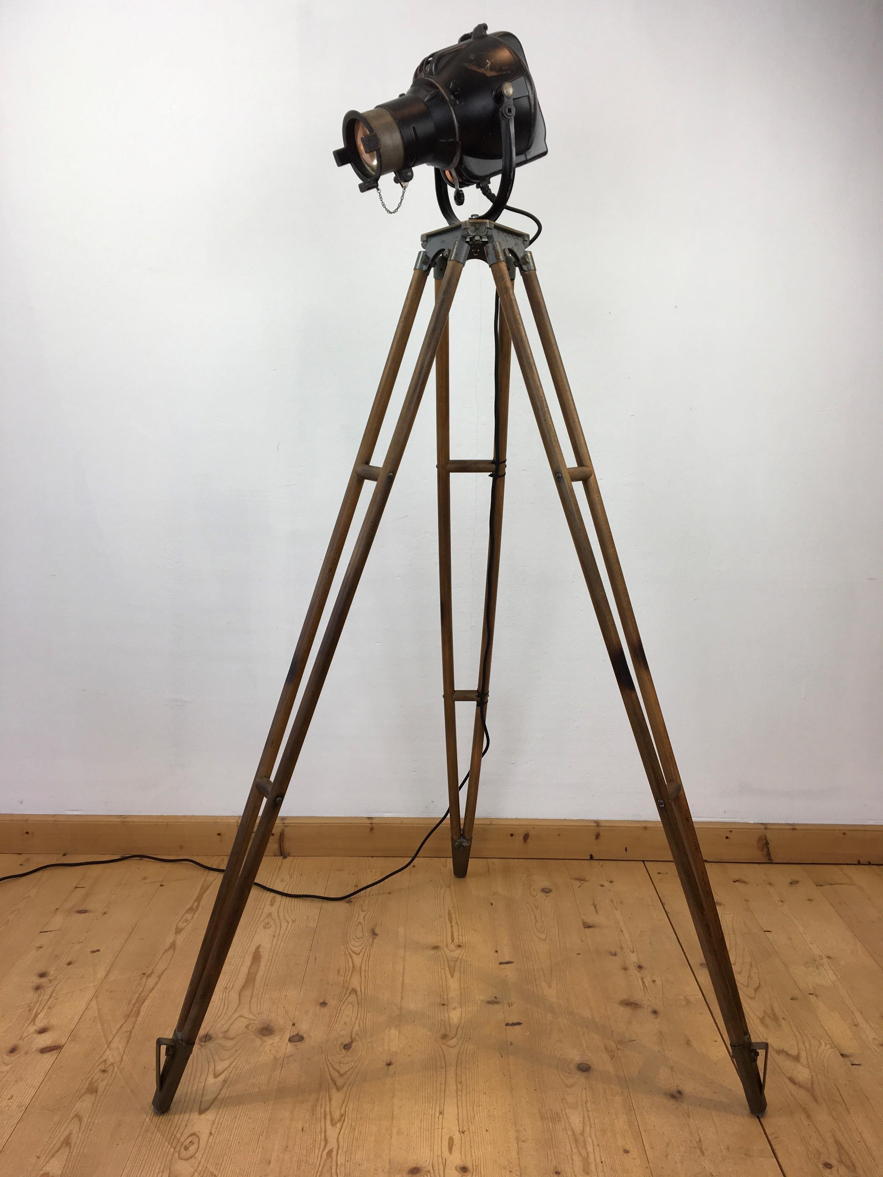Strand Electric theater spot - stage light on wooden tripod. 
This English spot - theatre projector light was made by Strand Electric Lighting Company and dates 1950 - 1960. 
It's an iconic design!
Strand Electric is an international theatre and