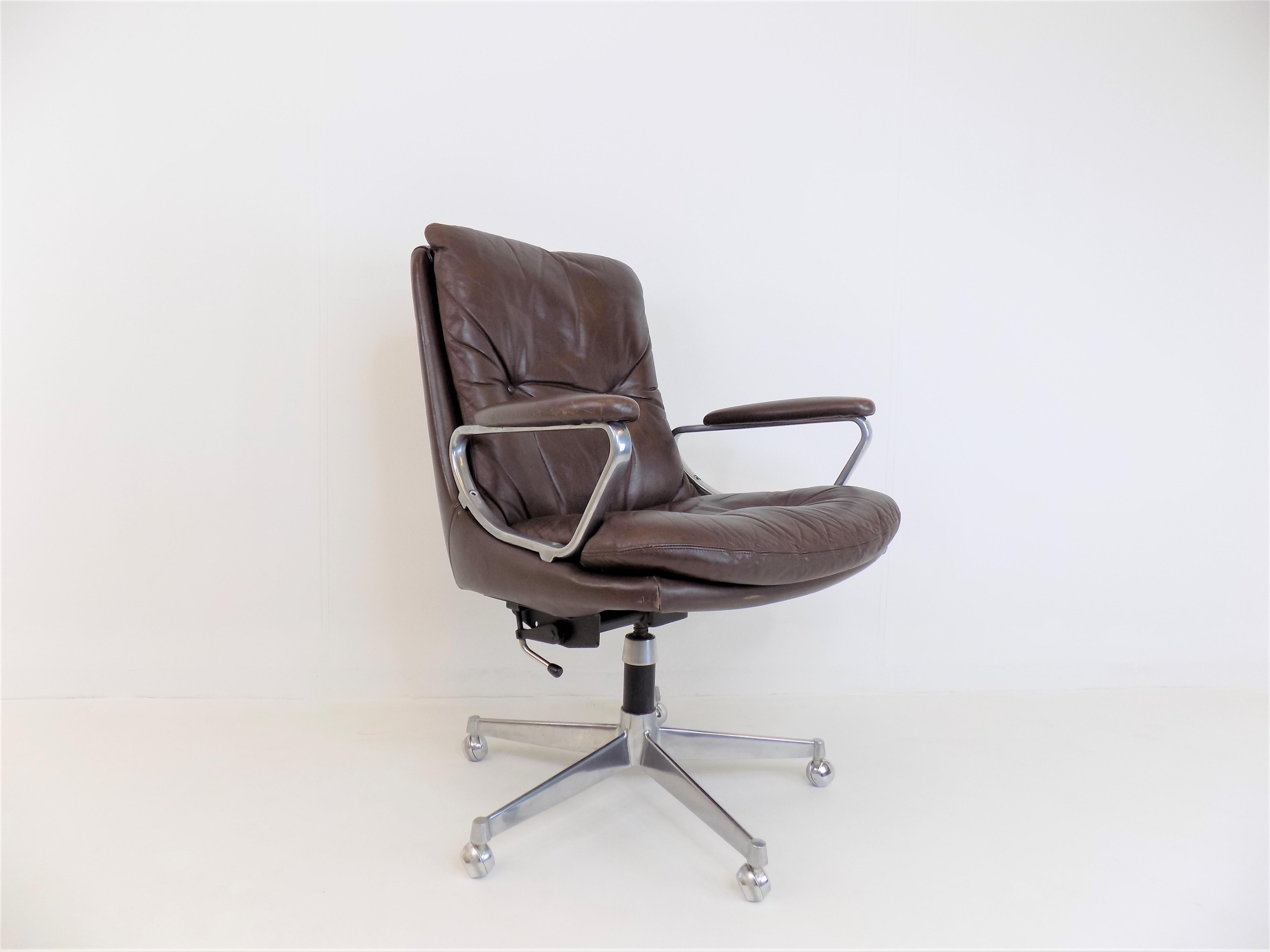 A Gentilina office chair in brown leather in good condition. The leather and the stainless steel backrests show slight signs of wear, especially on the armrests. The armchair has a height adjustment, with seat heights between 47 - 58 cm, through a