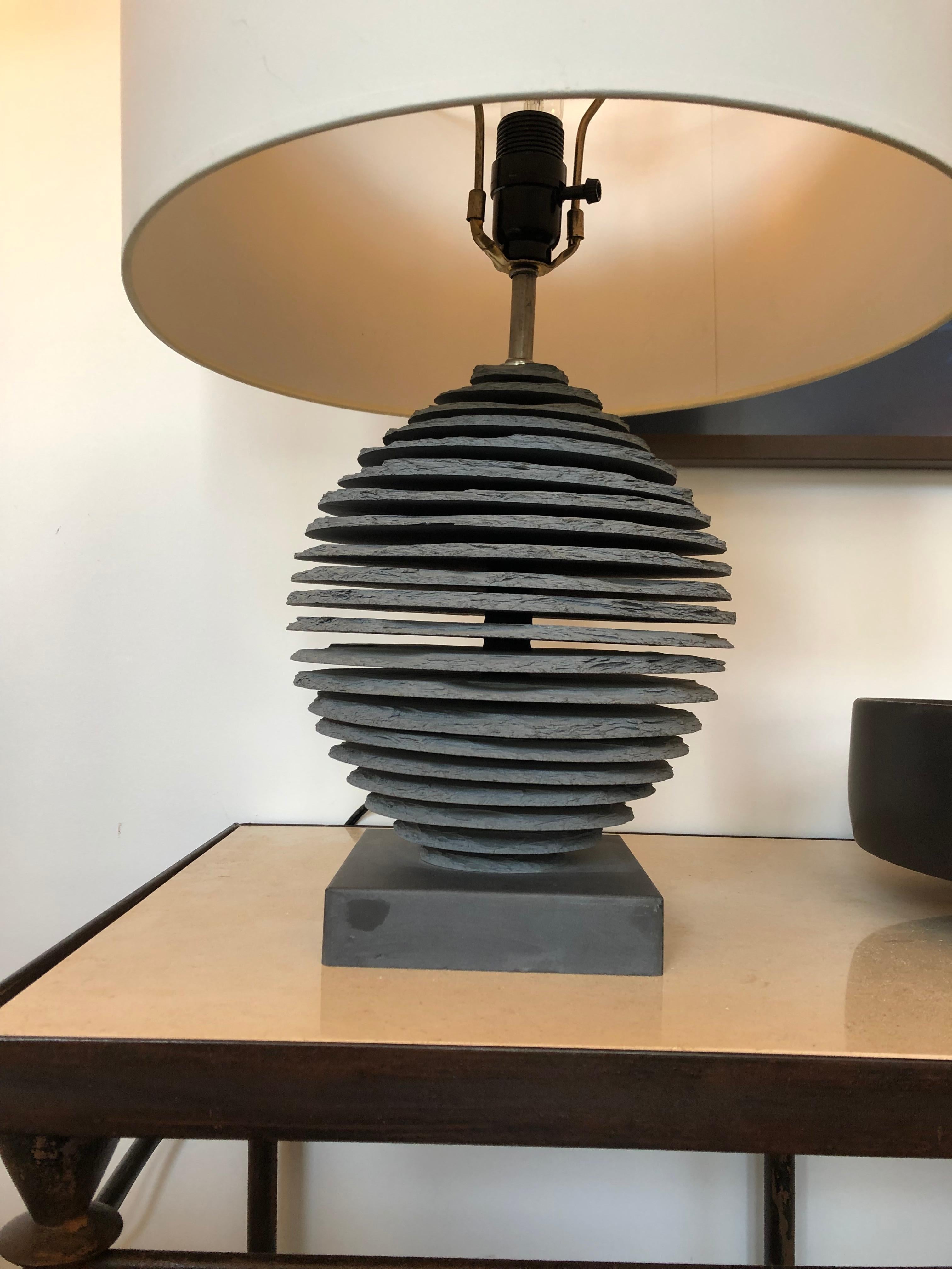 The lamp base is handcrafted with multiple individually carved sections of blue stone slate, then with mathematical precision is hand layered in horizontal parallel sections leaving space between each section creating an optic see through illusion.