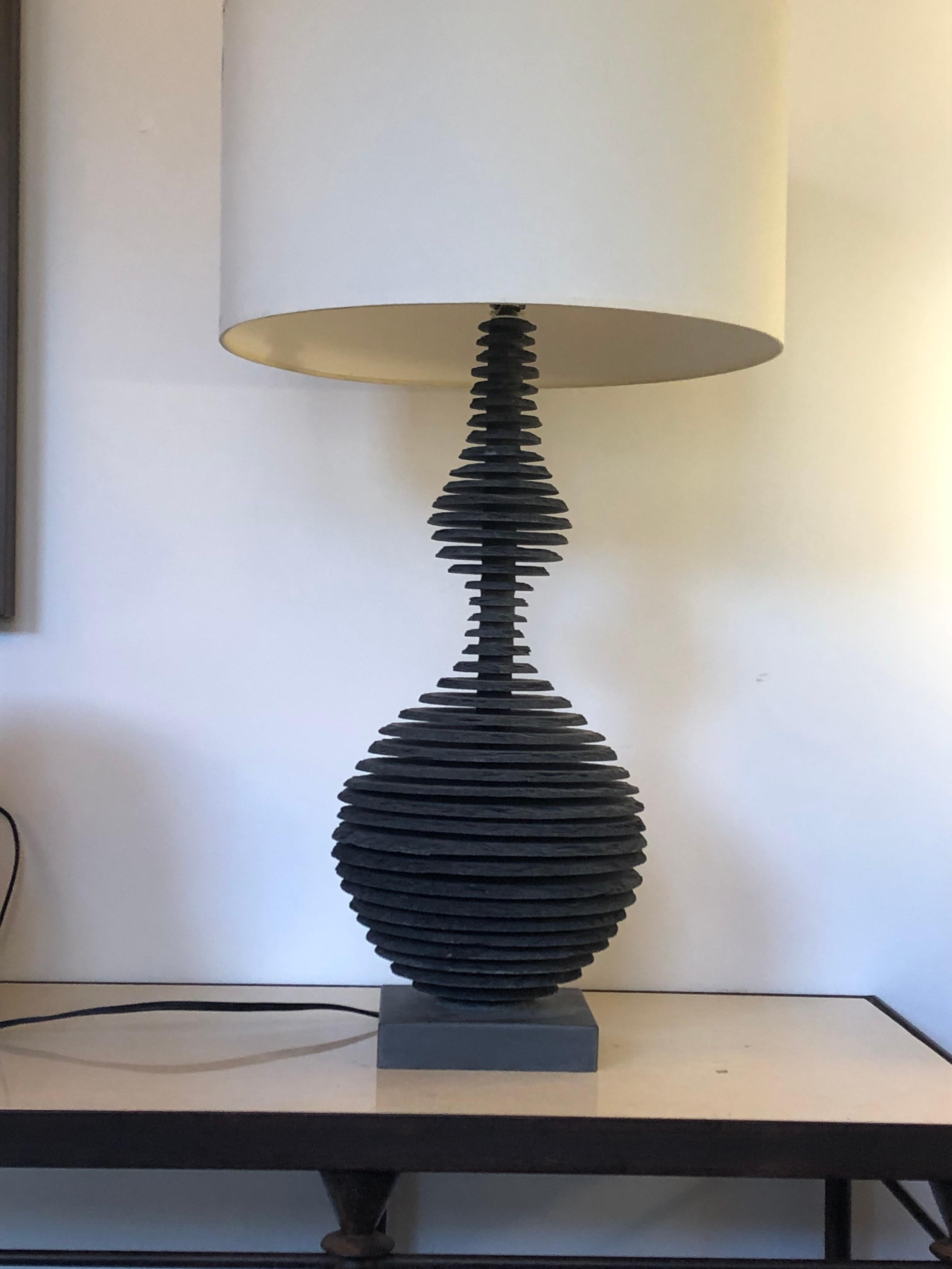 The lamp base is handcrafted with multiple individually carved sections of blue stone slate, then with mathematical precision is hand layered in horizontal parallel sections leaving space between each section creating an optic see through illusion.