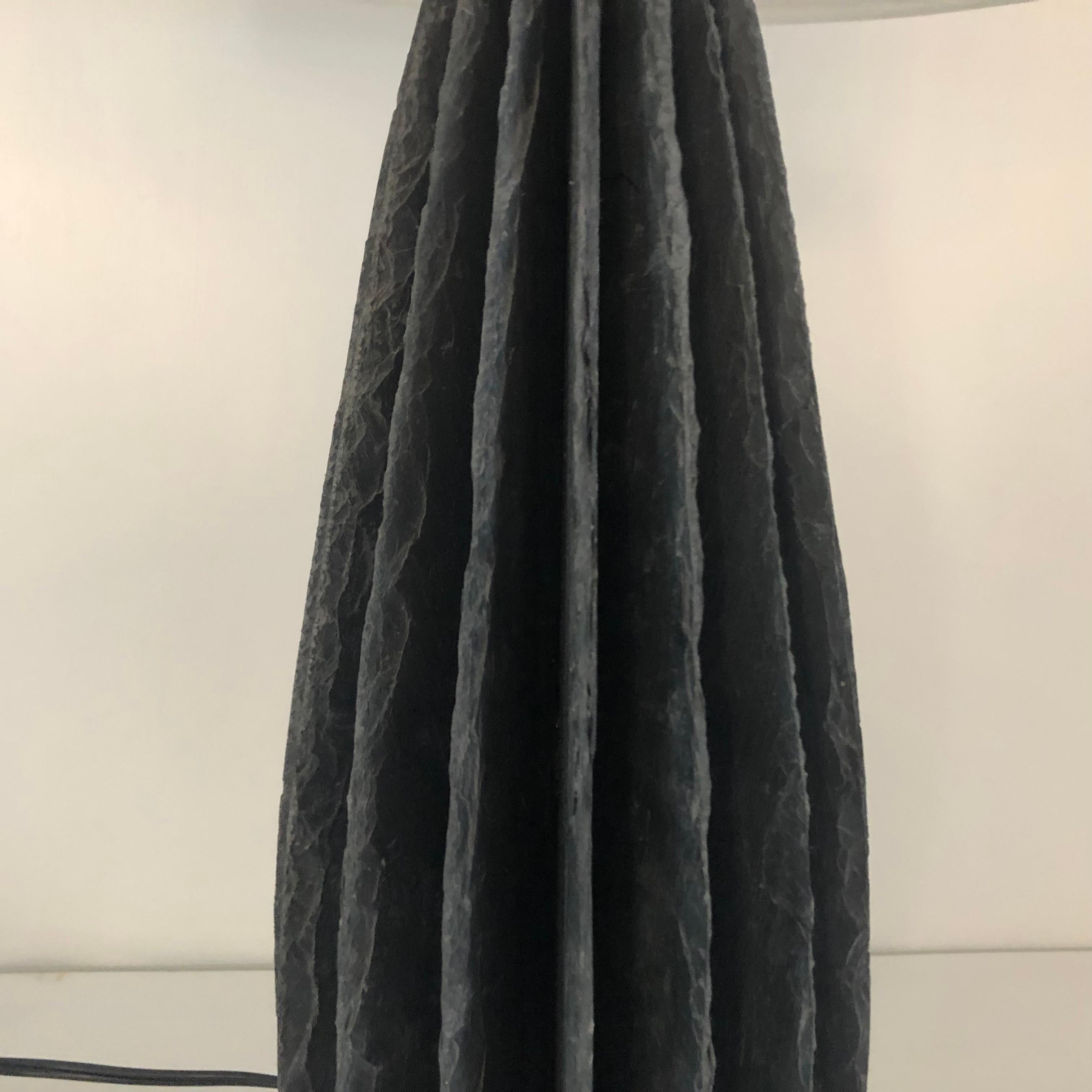La base della lampada è realizzata a mano utilizzando diverse sezioni di ardesia blu scolpite singolarmente; ogni sezione viene poi incastonata sulla verticale in una configurazione a ventaglio che crea la base scultorea della lampada. Questa