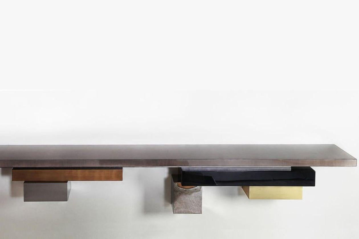 Stratos L, Console - Wall mounted from the STRATOS LINE
The asymmetrical composition for this console is a wild yet harmonious combination of several metals, wood and lacquer.

Materials: 
Tinted Gray Sycamore 100 % glossy
Hand patinated silver and