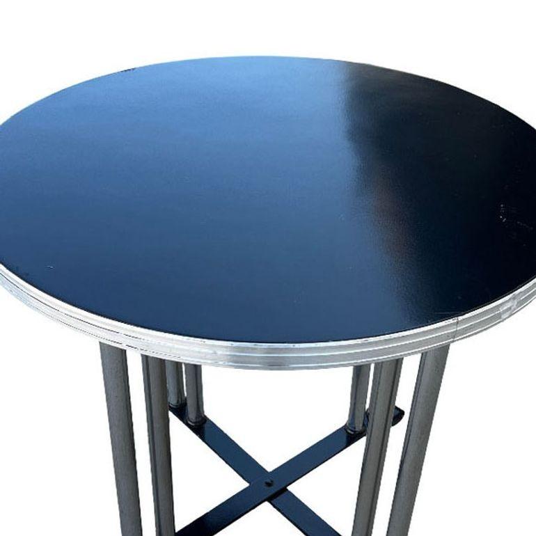 Von Wolfgang Hoffmann inspirierter runder Beistelltisch mit stromlinienförmigem Design, das durch die gerillte Chromleiste, die verchromten Stahlbeine und den geschwungenen Fuß aus schwarzer Emaille hervorgehoben wird. Die schwarze Kompositplatte