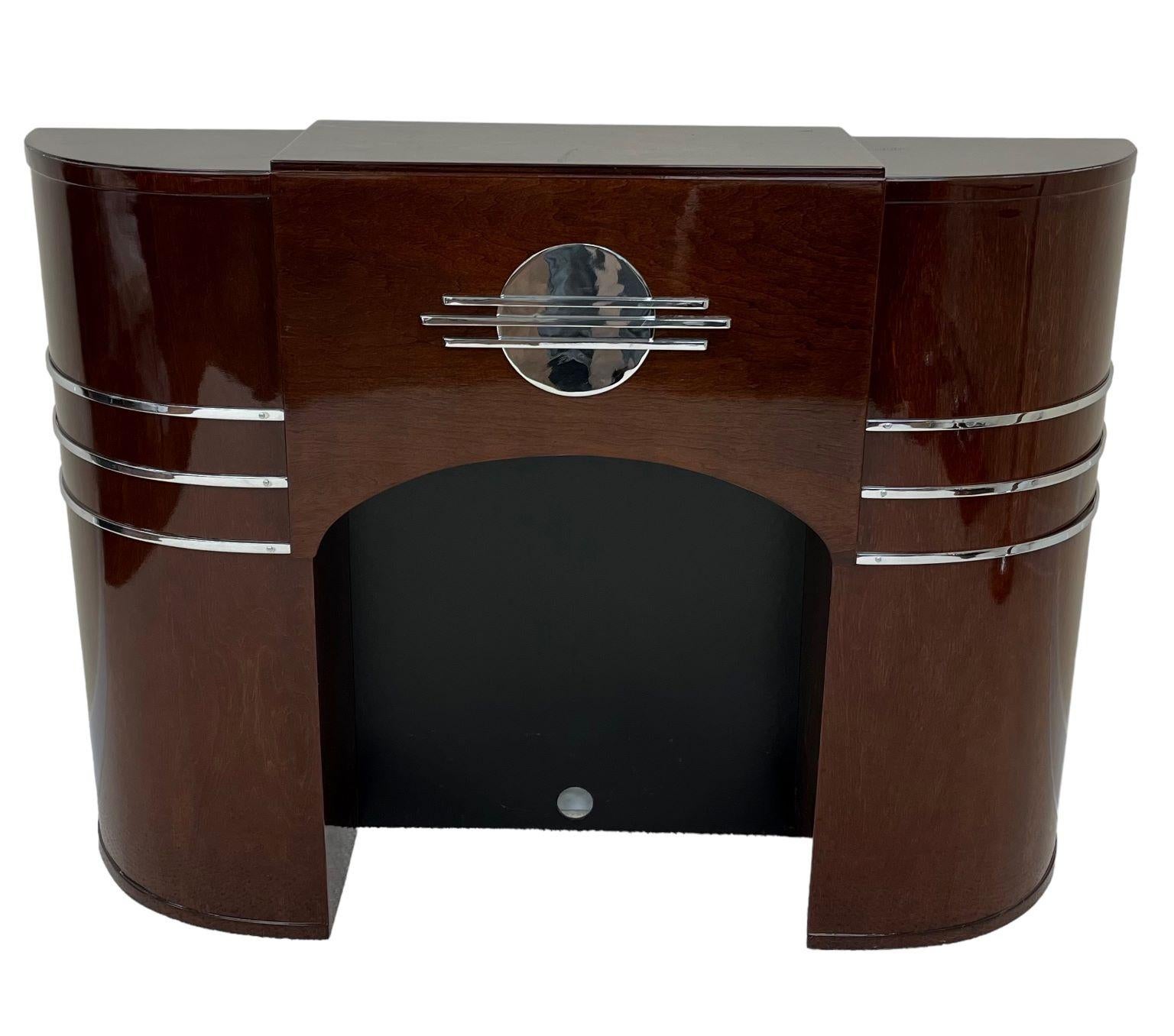 Rare Art Deco streamline faux fireplace mantle. Remarkable craftsmanship and great detail with the polished chrome accents. Professionally restored in maple stained mahogany. Dimensions 54 inches wide by 12 inches deep and 40 inches high.
