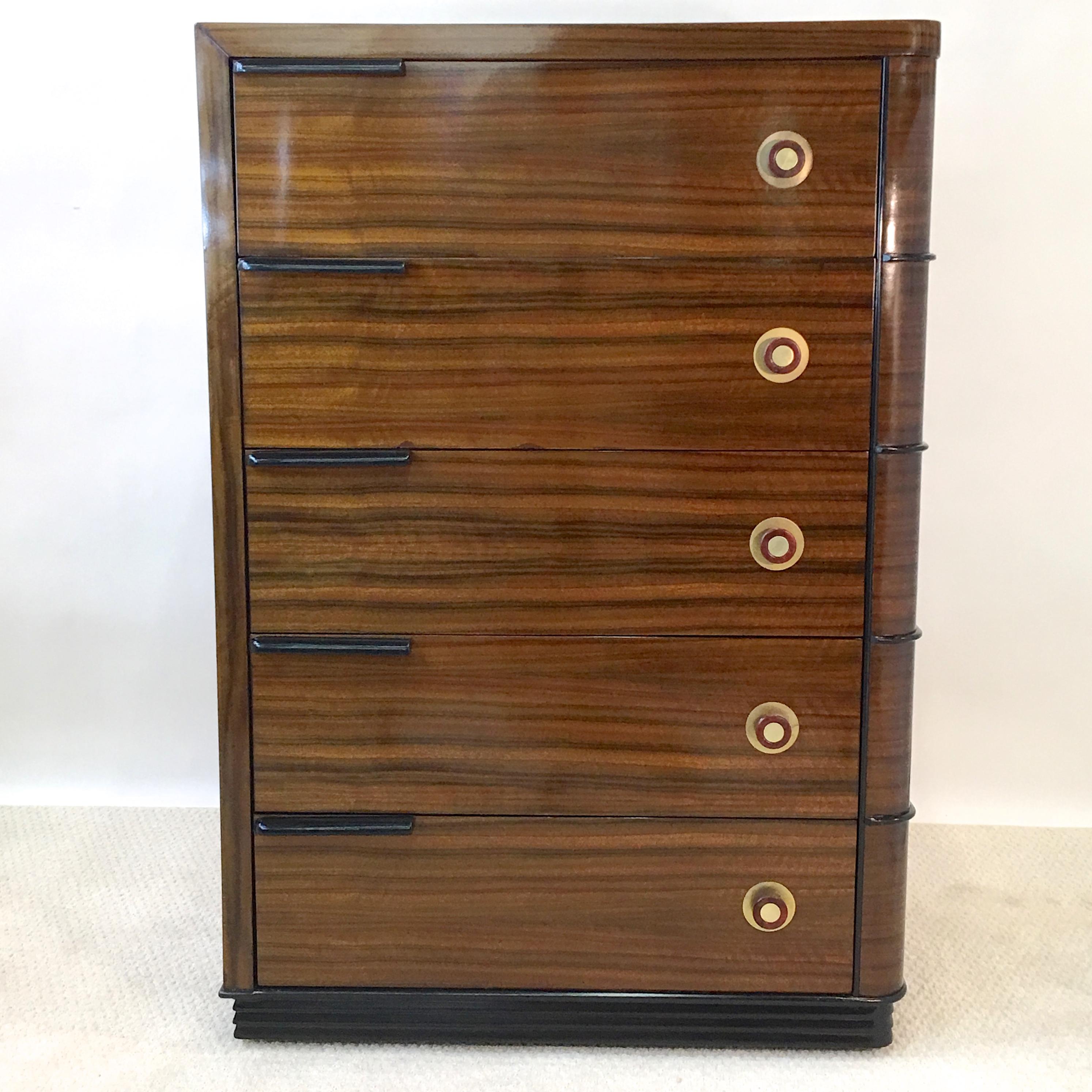 1930s streamline Art Deco beautifully grained walnut five-drawer tall dresser with round brass and bakelite drawer pulls and ebonized horizontal stylings, in the manner of Gilbert Rohde and Donald Deskey.

Beautifully restored in high gloss