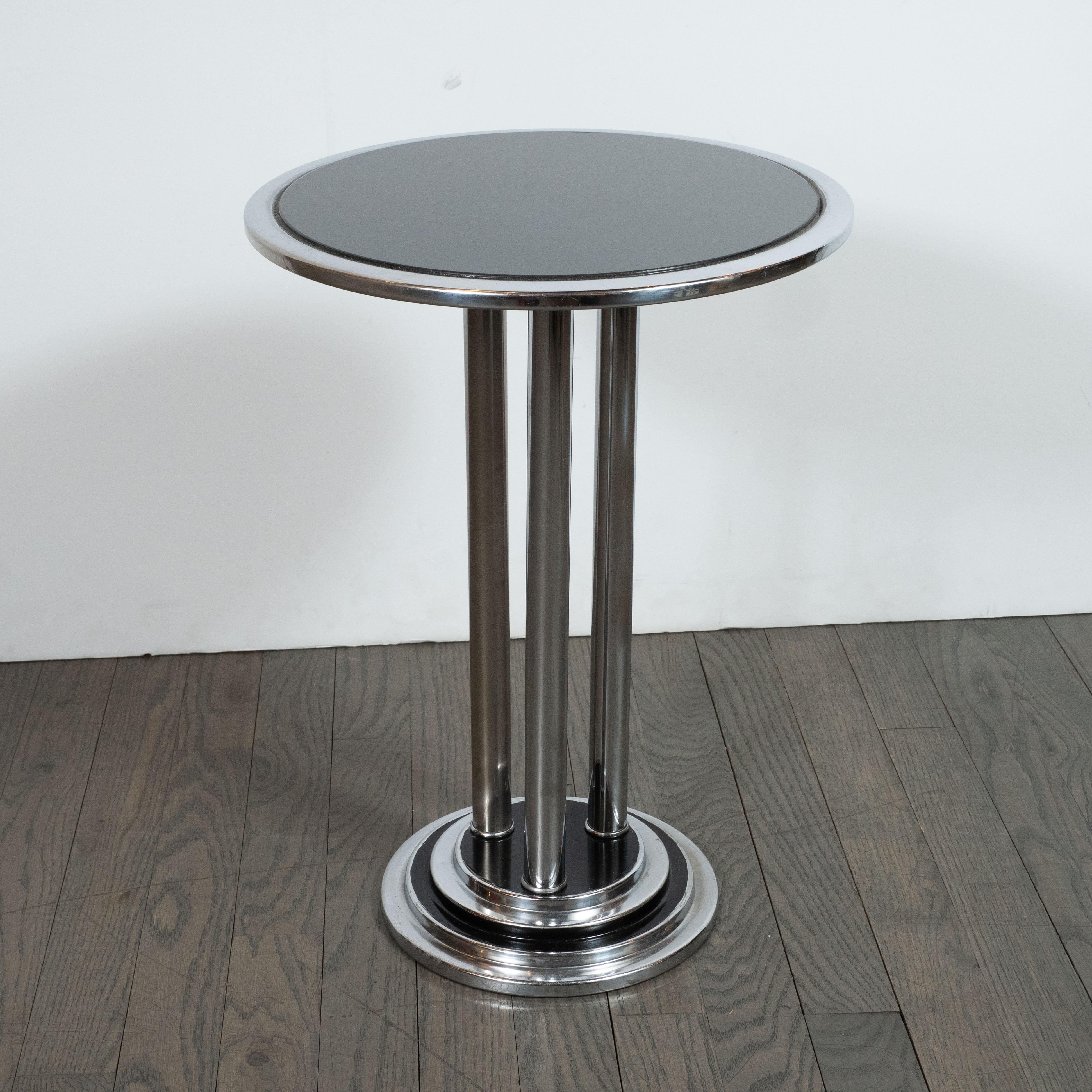 This sophisticated Machine Age Art Deco side table was designed in the United States, circa 1935. The table has a four-tier, stepped circular base. The tiers alternate between lustrous chrome and a high-gloss black enamel. Three chrome columns sit