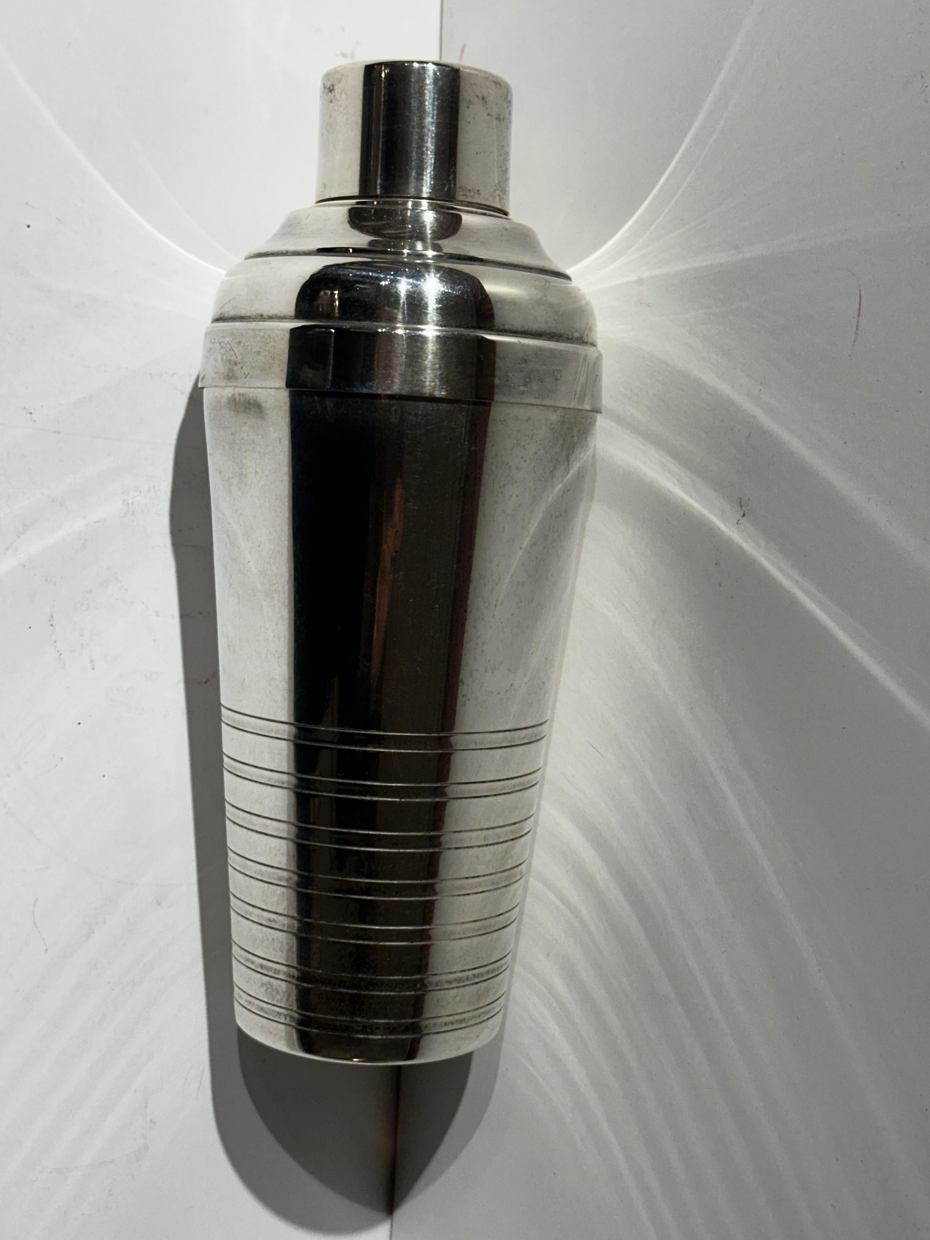 Stromlinienförmiger Cocktail Shaker, elegant in seiner Schlichtheit mit geätzten Geschwindigkeitslinien am Boden und einer glänzenden Silberoberfläche. Es gibt ein eingebautes Sieb und der Shaker wurde im klassischen französischen Stil hergestellt.