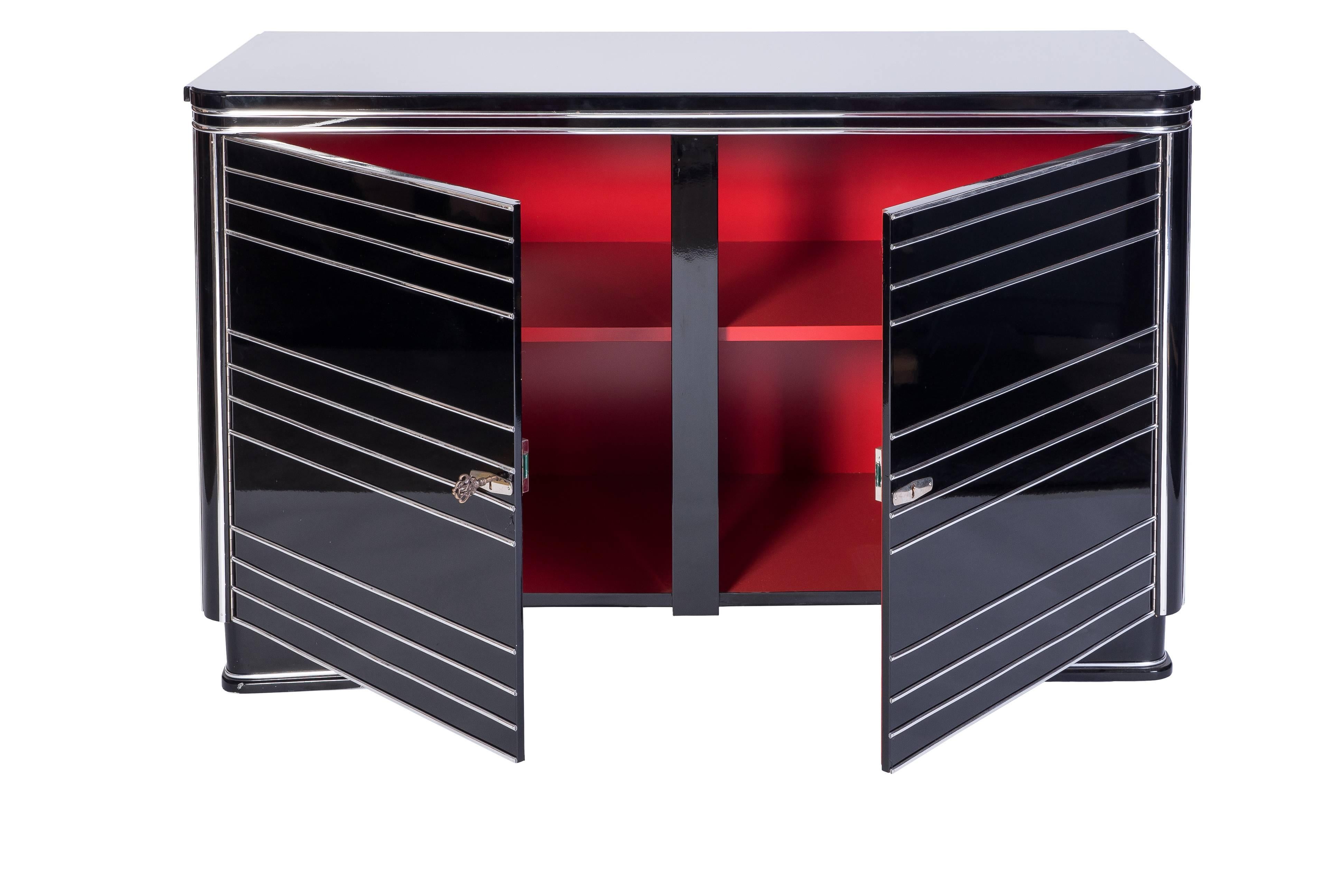 This French Art Deco commode features a streamlined design with chrome lines cascading throughout the entire piece, with chrome applications on the doors, a cherry red interior and a high gloss black lacquer exterior.

Made in France, circa
