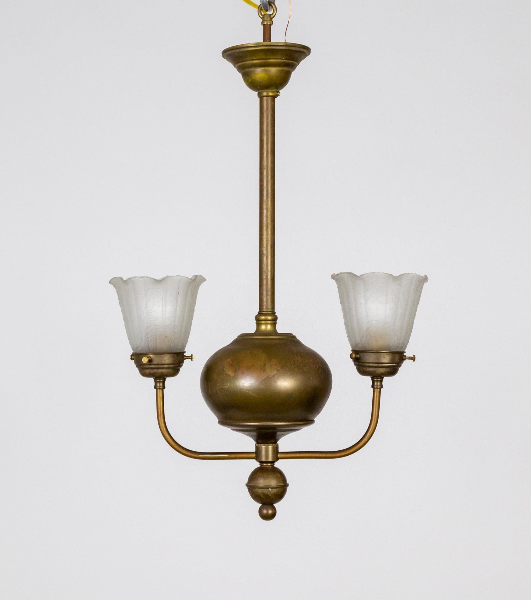 A brass ball is the streamlined, main body of this well proportioned, pendant style chandelier with two slim, upward facing arms. With pleasing brass patina and Victorian, embossed, frosted glass, flower shades. Newly wired. 2 medium base sockets.