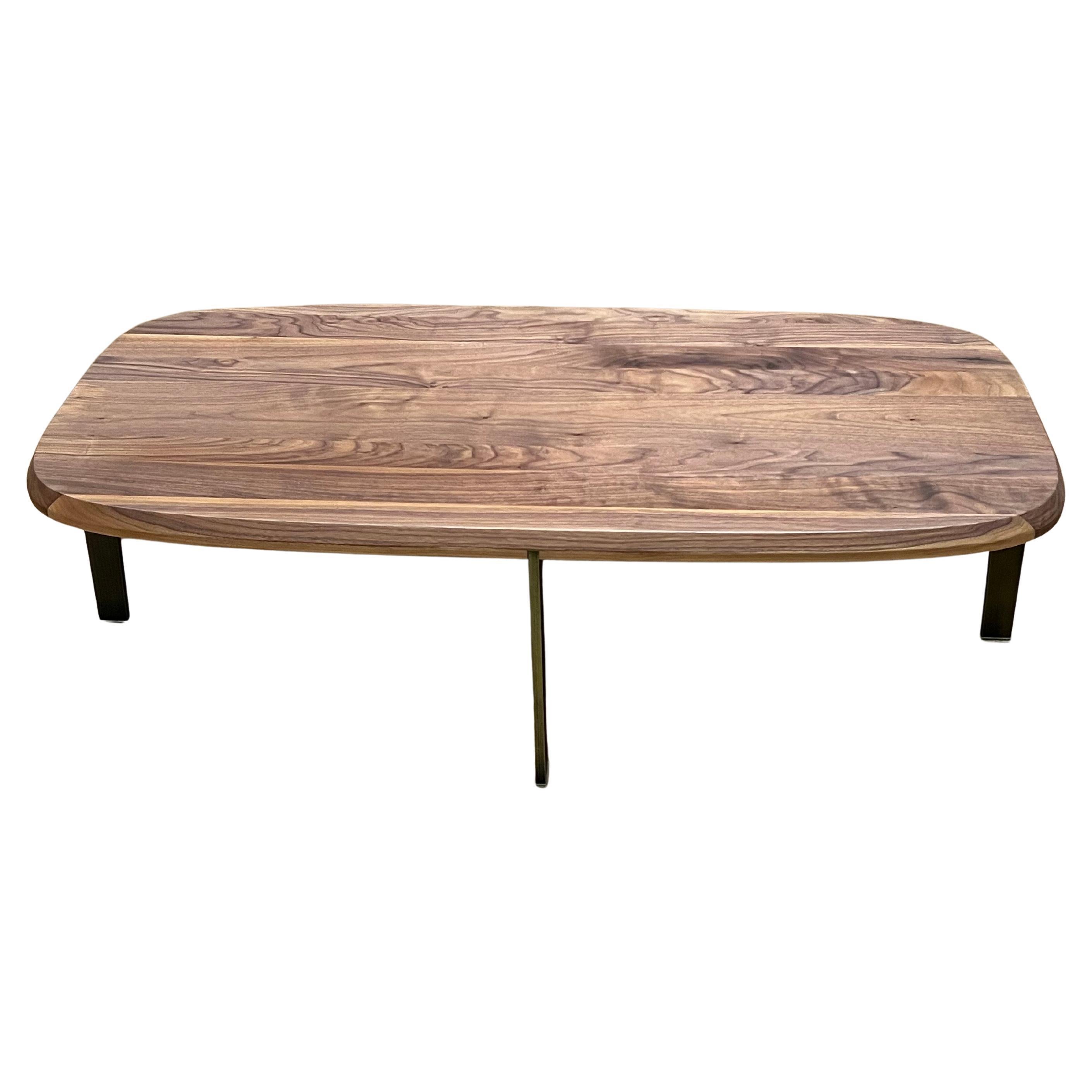 Table basse minimaliste contemporaine en noyer massif avec coins arrondis et pieds en bronze patiné avec embouts en plastique transparent, solide et robuste en excellent état. Né au Danemark en 1943, le designer Niels Bendtsen a émigré avec sa