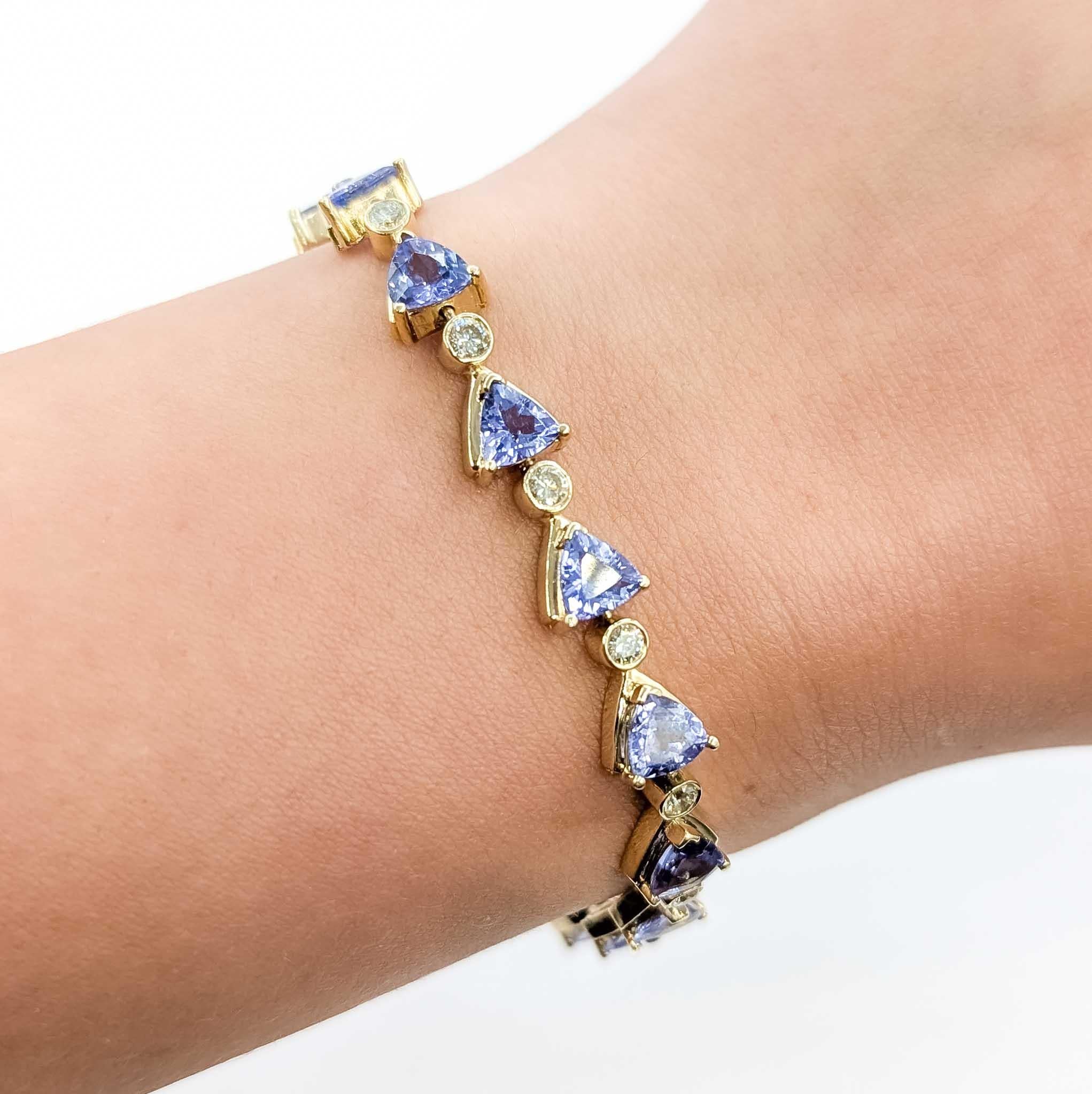 Esta excepcional pulsera está elaborada en oro amarillo de 14 quilates y muestra una vibrante combinación de tanzanita y diamantes. Con 9,18 quilates de gemas de tanzanita talla trillante de ricos matices, alternadas con diamantes brillantes