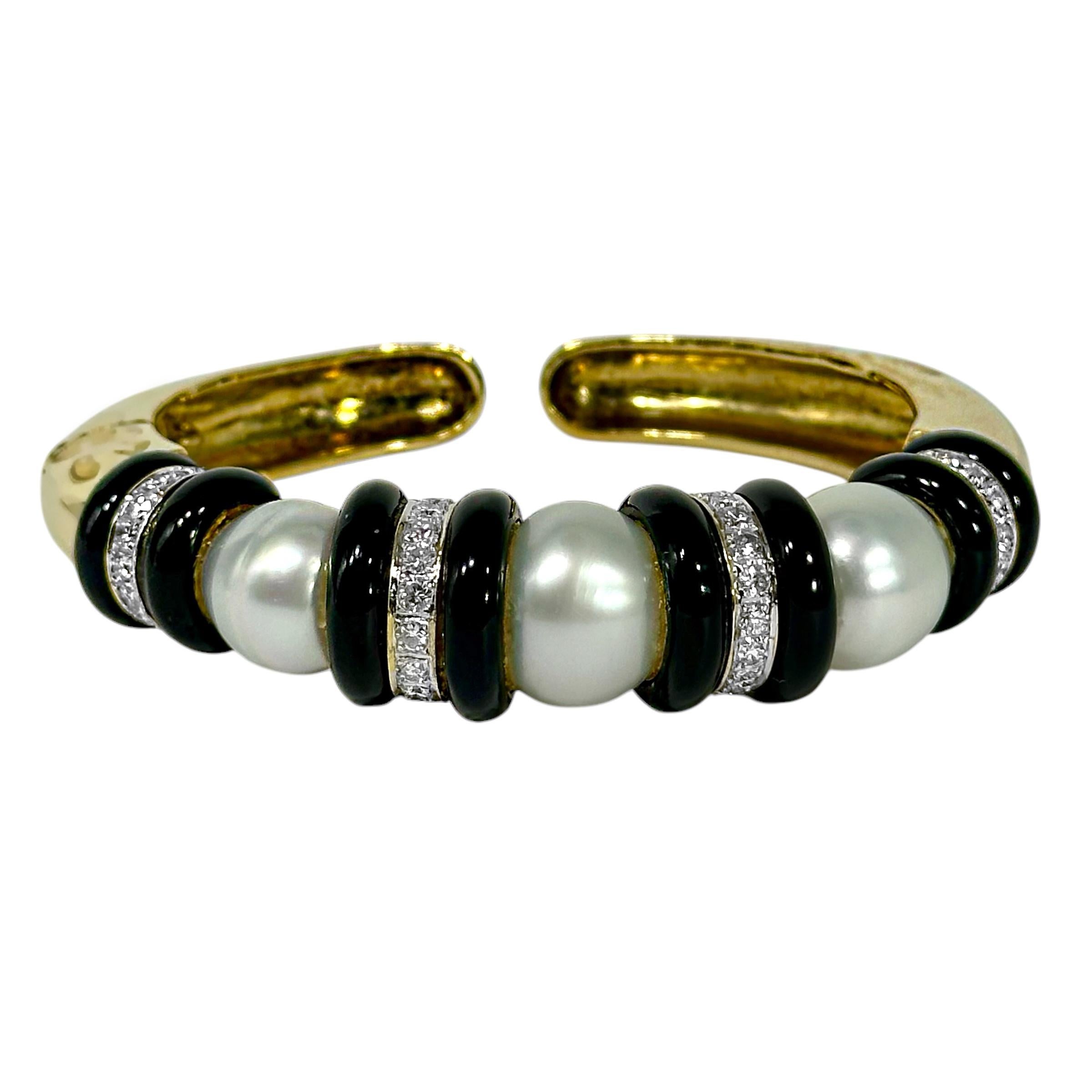 This dramatic, vintage bangle bracelet is set with three large South Sea cultured pearls measuring from 12mm to 14mm, flanked four diamond and black onyx stations. The forty eight diamonds weigh a total of approximately 2.35ct of overall H/I color