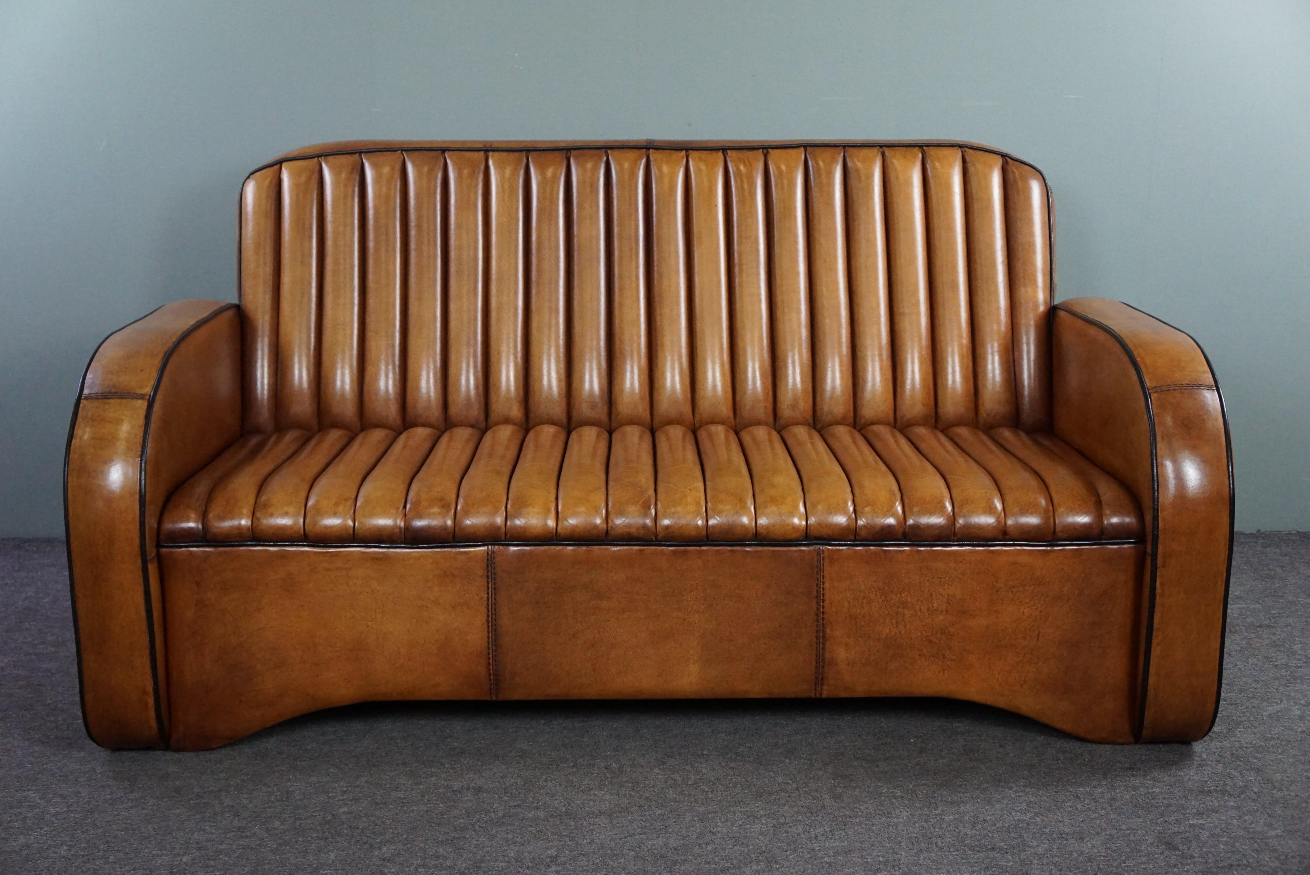 Offered is this hand-patinated cognac-colored sofa made of beautiful sheep leather.

This 2.5-seater sofa is beautifully upholstered with sheep leather and hand patinated in a warm cognac color. The sofa is finished with black piping along the