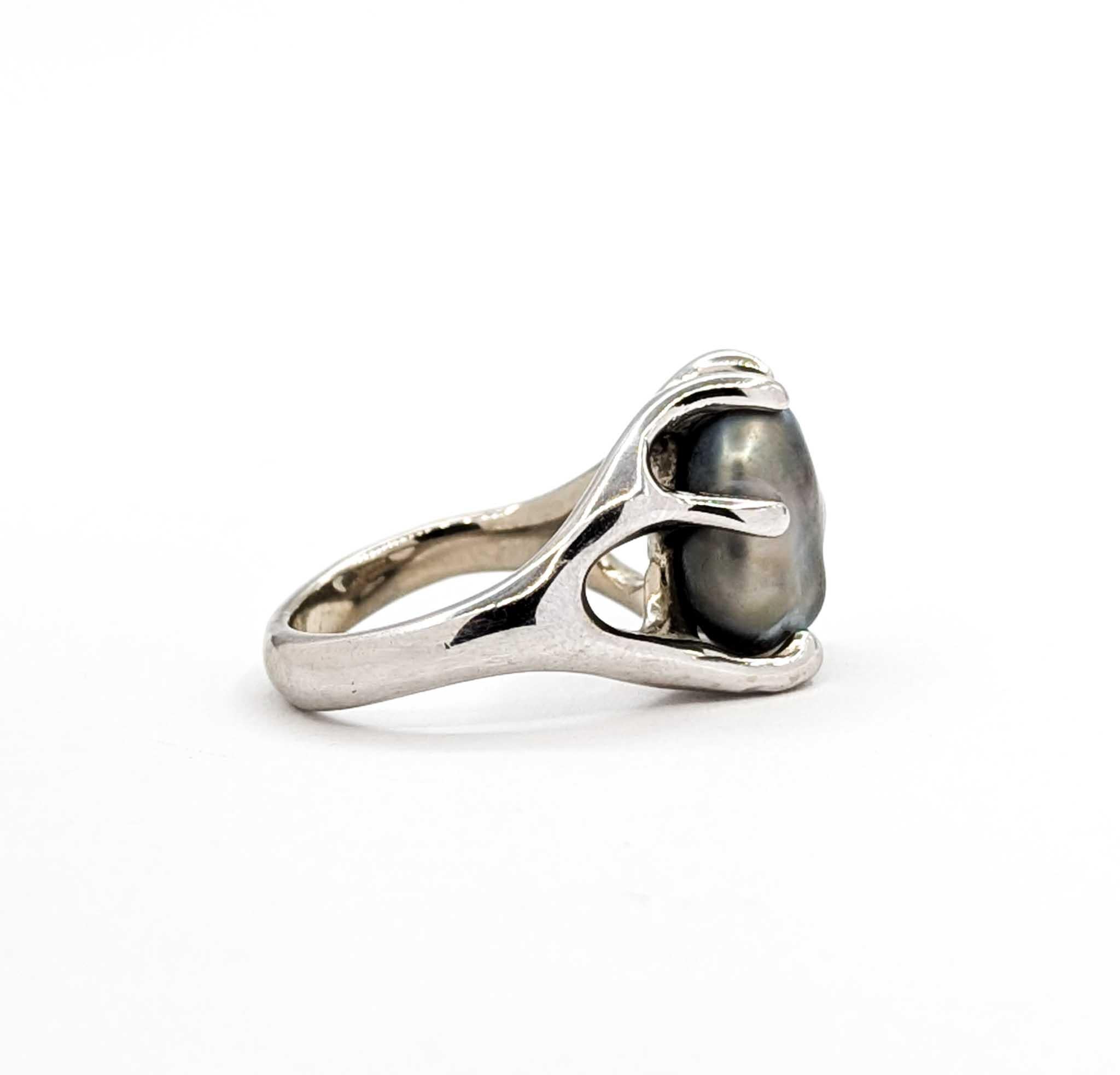 Cette bague frappante présente une perle baroque audacieuse de 12,6 x 11 mm, solidement sertie dans une monture sculpturale en or blanc 14k. Les contours organiques de la perle présentent des nuances irisées de gris, d'argent et d'or doux, mettant