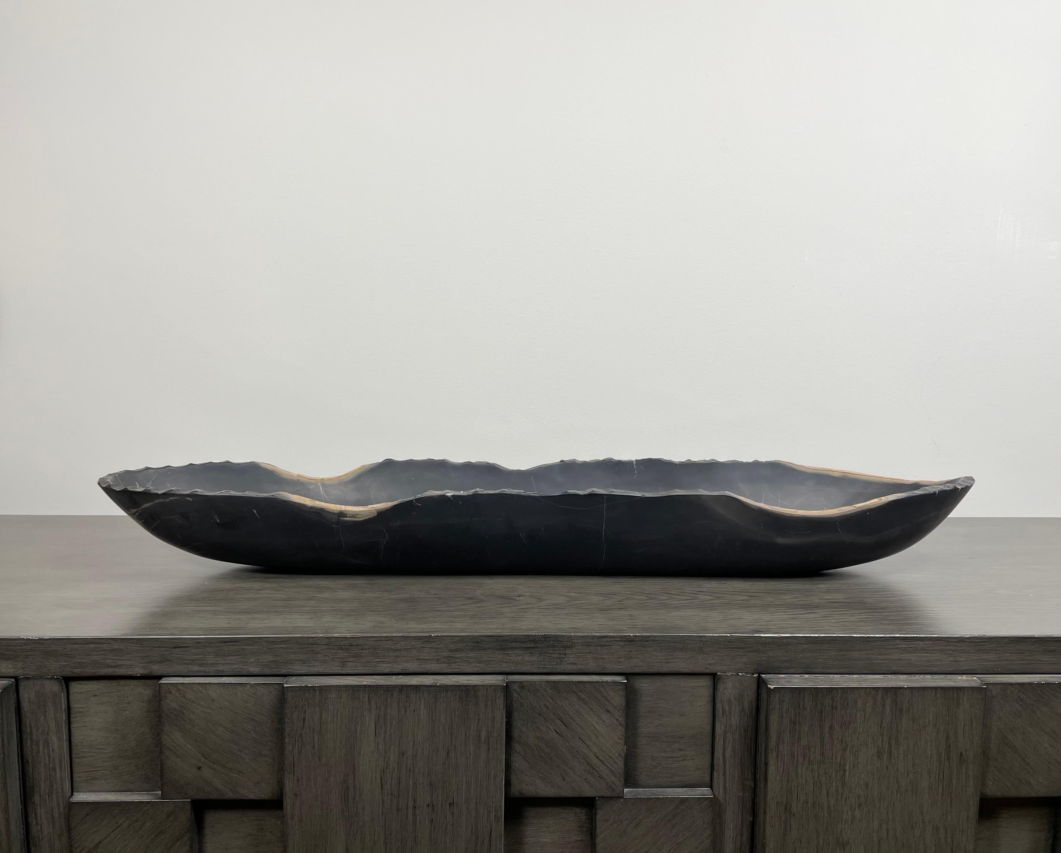 A striking black oblong marble bowl with a raw edge. This large bowl has a matte finish and the contrasting edge in earth tones. This one of a kind decorative vessel is meticulously hand-carved from a single piece of marble by skilled artists. This