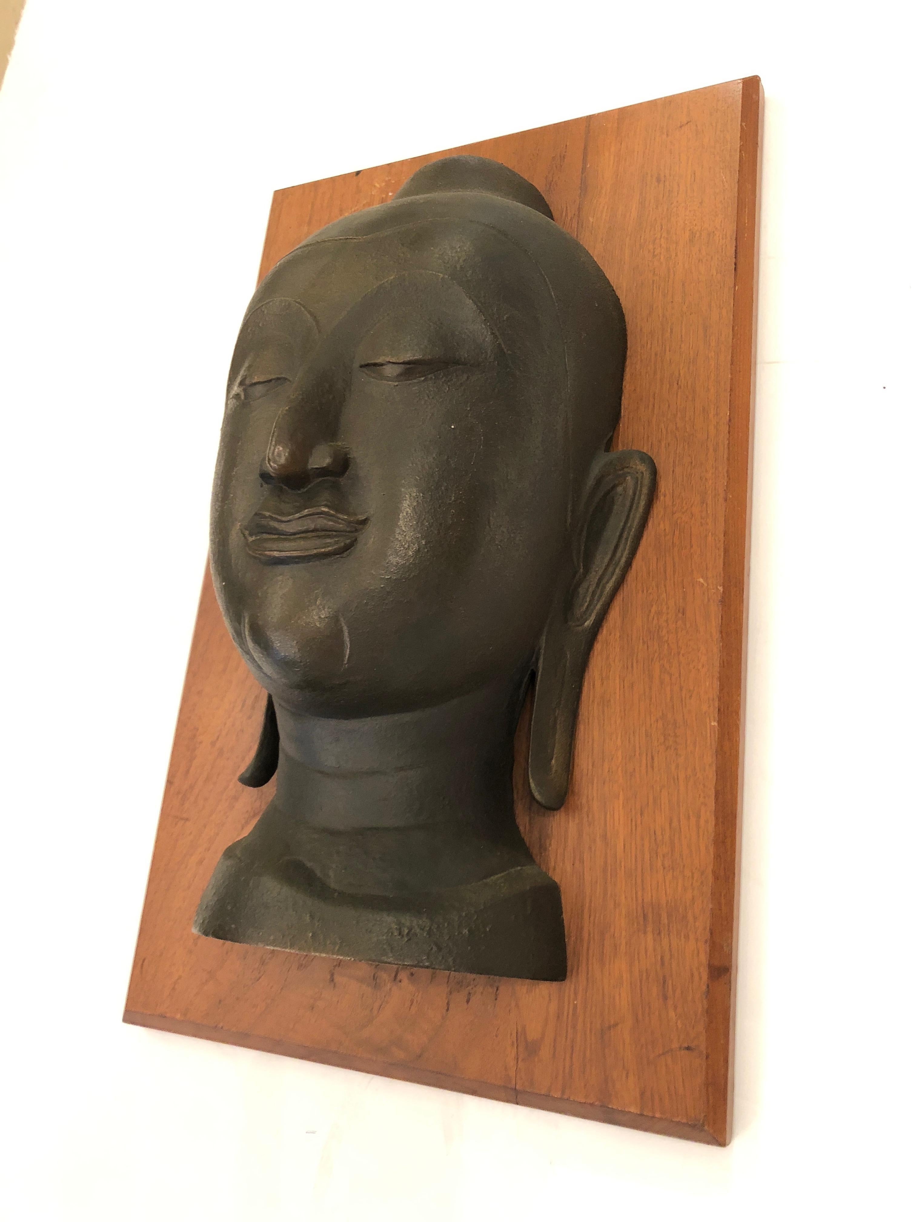 A striking wall sculpture having a serene bronze Buddha head mounted on handsome walnut board.