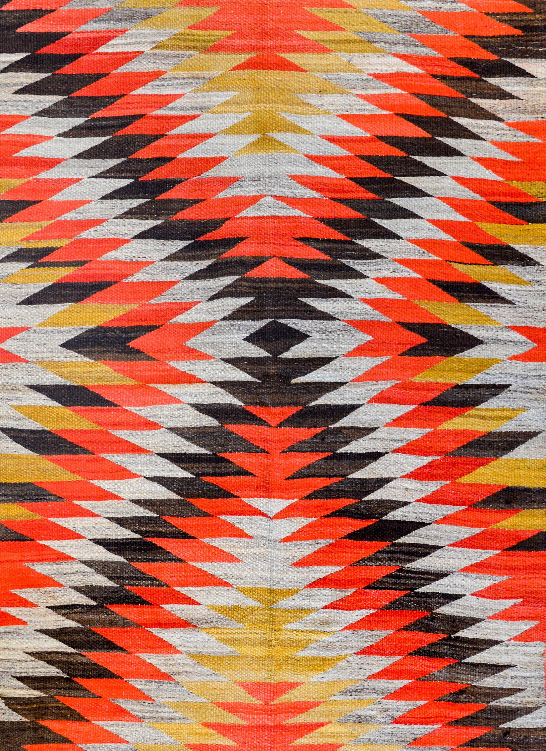 A striking early 20th century native North American Navajo rug with a fabulous pattern containing myriad triangles creating a larger triangle pattern, all woven in crimson and gold vegetable dyed wool, with black and grey undyed wool.