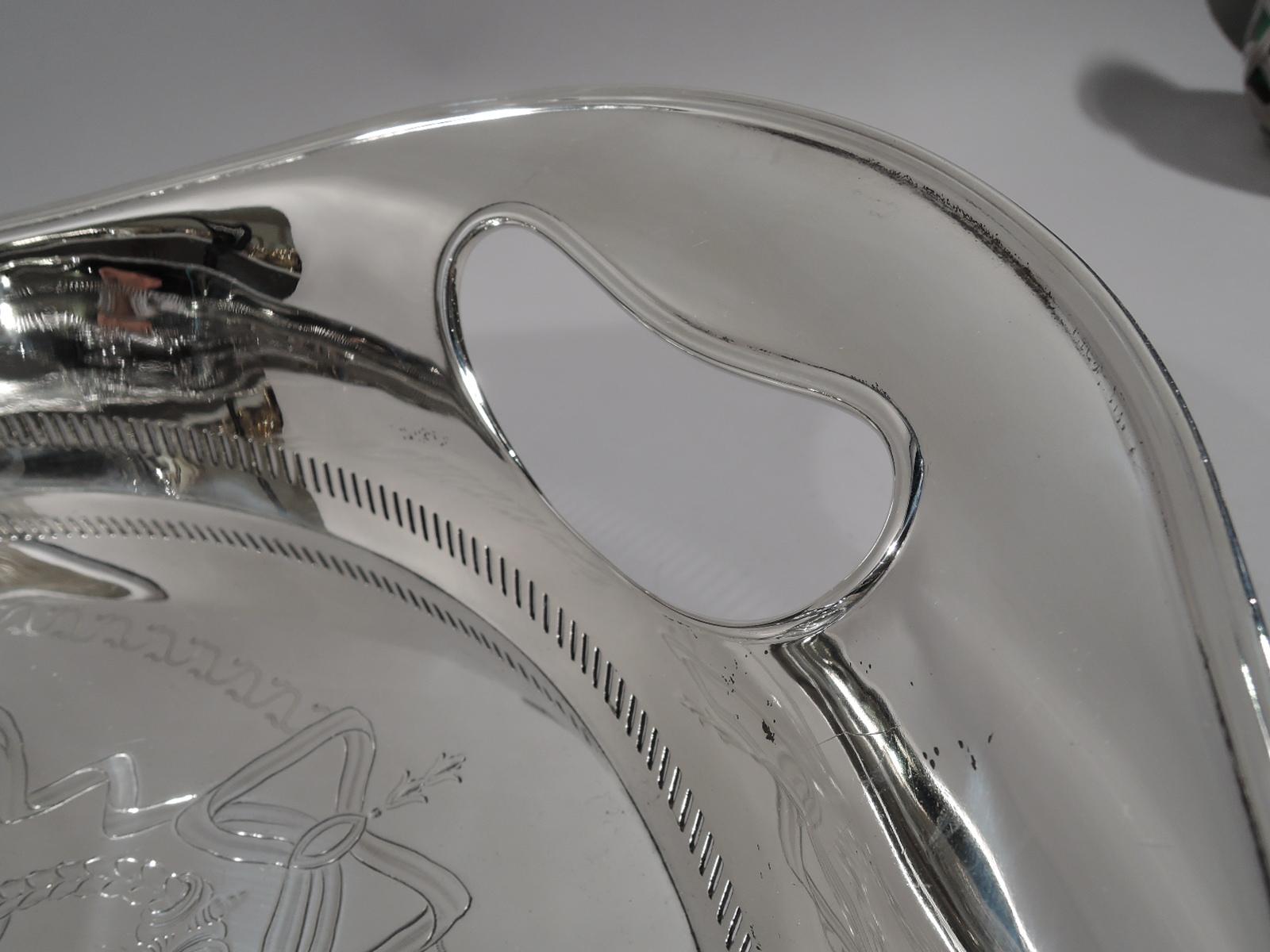 Striking Edwardian sterling silver tea tray. Made by Hawksworth, Eyre & Co., Ltd in Sheffield in 1910. Oval well engraved with bold Regency ornament, ribbon-tied oval frames joined by garlands in Vitruvian scroll border. Sides plain with gallery