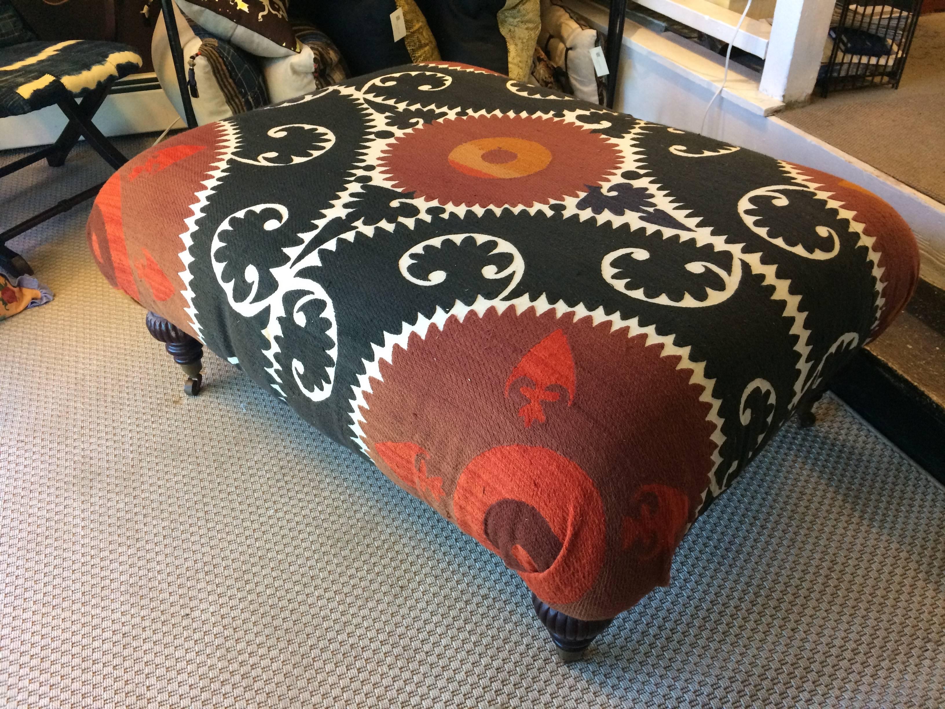 A large comfy ottoman or coffee table having wooden turned legs and fabulously graphic upholstery that's an antique central Asian dowry cloth, handmade in black, white, and two shades of orange/red.