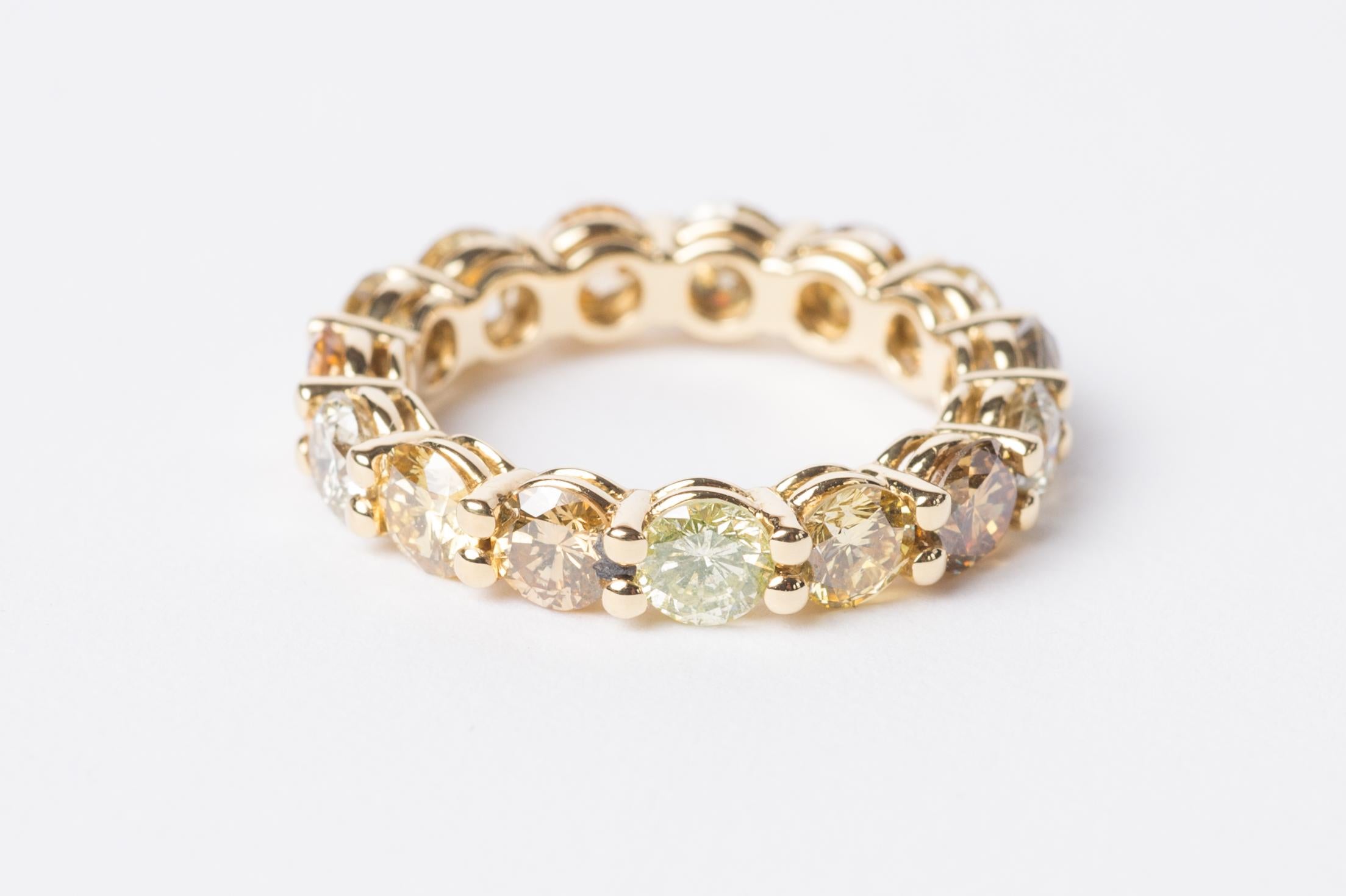 This classic yet modern eternity ring features differently coloured fancy diamonds in rich, earthy tones, making it a unique piece full of warmth and love. The brown, yellow and grey stones in round brilliant cuts are arranged on a yellow gold band