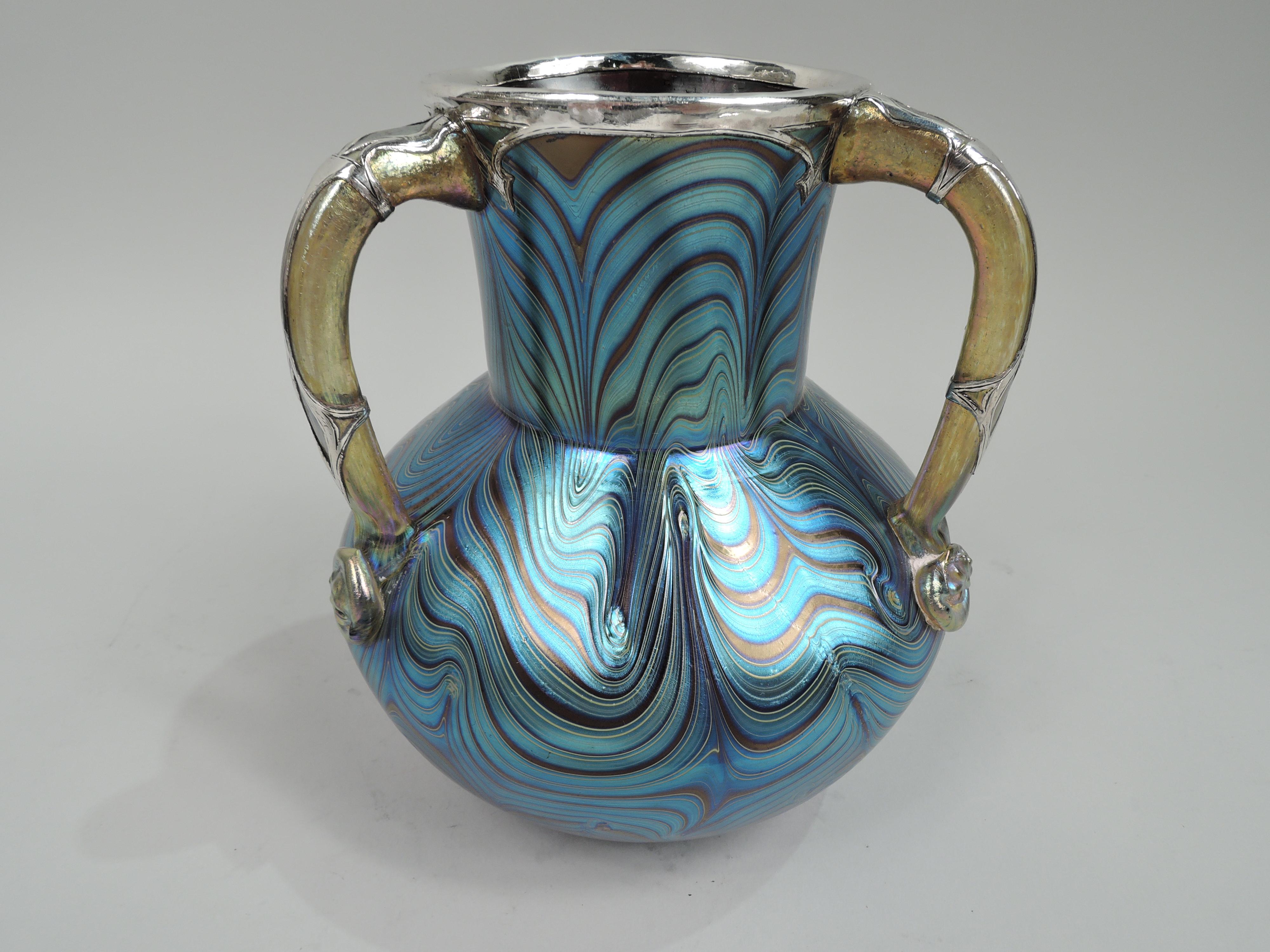 Striking turn-of-the-century Art Nouveau glass vase by historic Loetz with silver overlay. Globular with drum neck and wavy irregular pattern in iridescent blue heightened with purple and yellow. Interior red. Three gilt scroll handles with patera