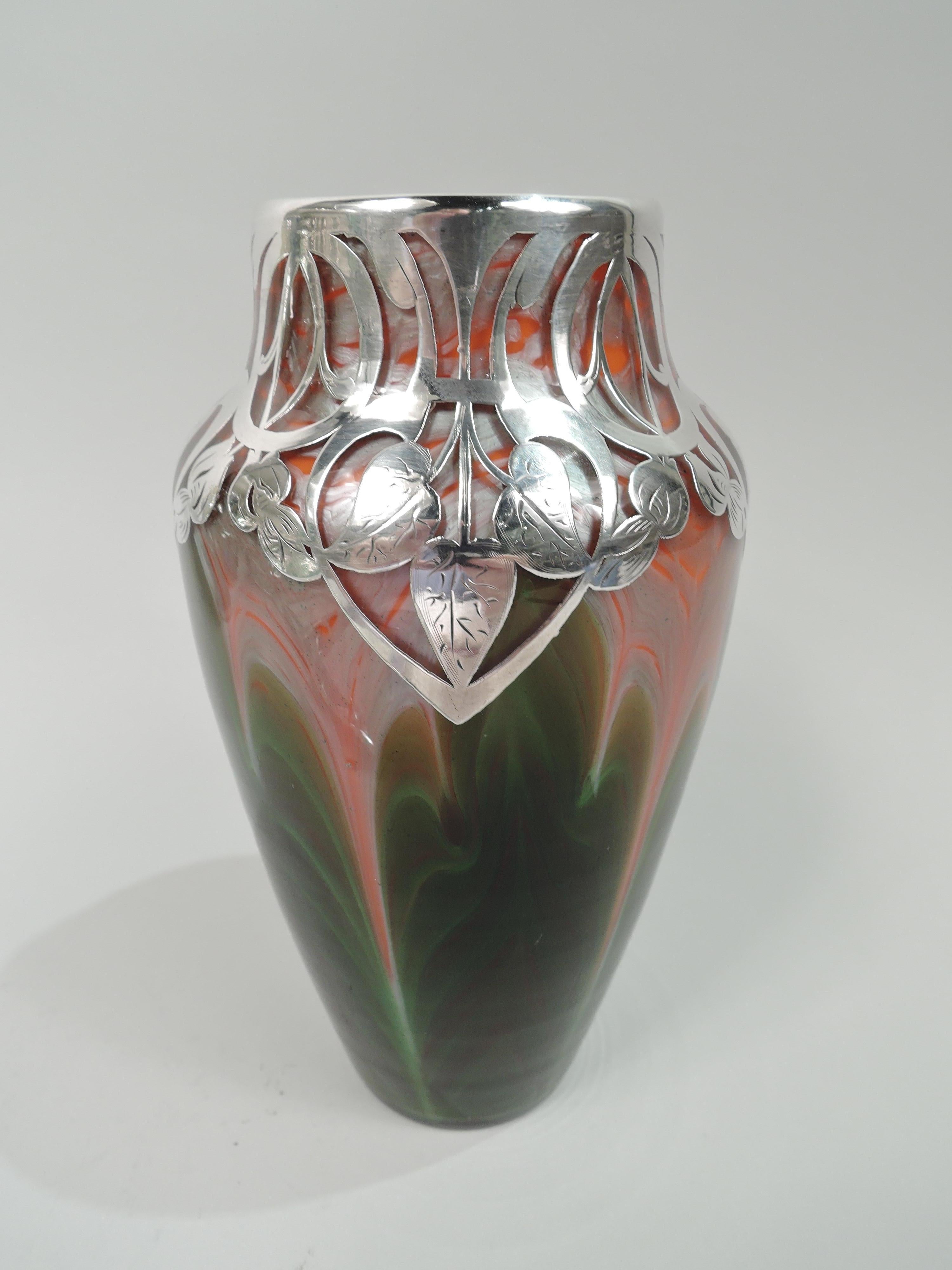 Striking turn-of-the-century glass vase by historic Loetz with engraved silver overlay. Ovoid with short and inset neck. Jugendstil-style overlay in controlled geometric pattern with circles and ovals as well as stylized leaves. Glass is iridescent