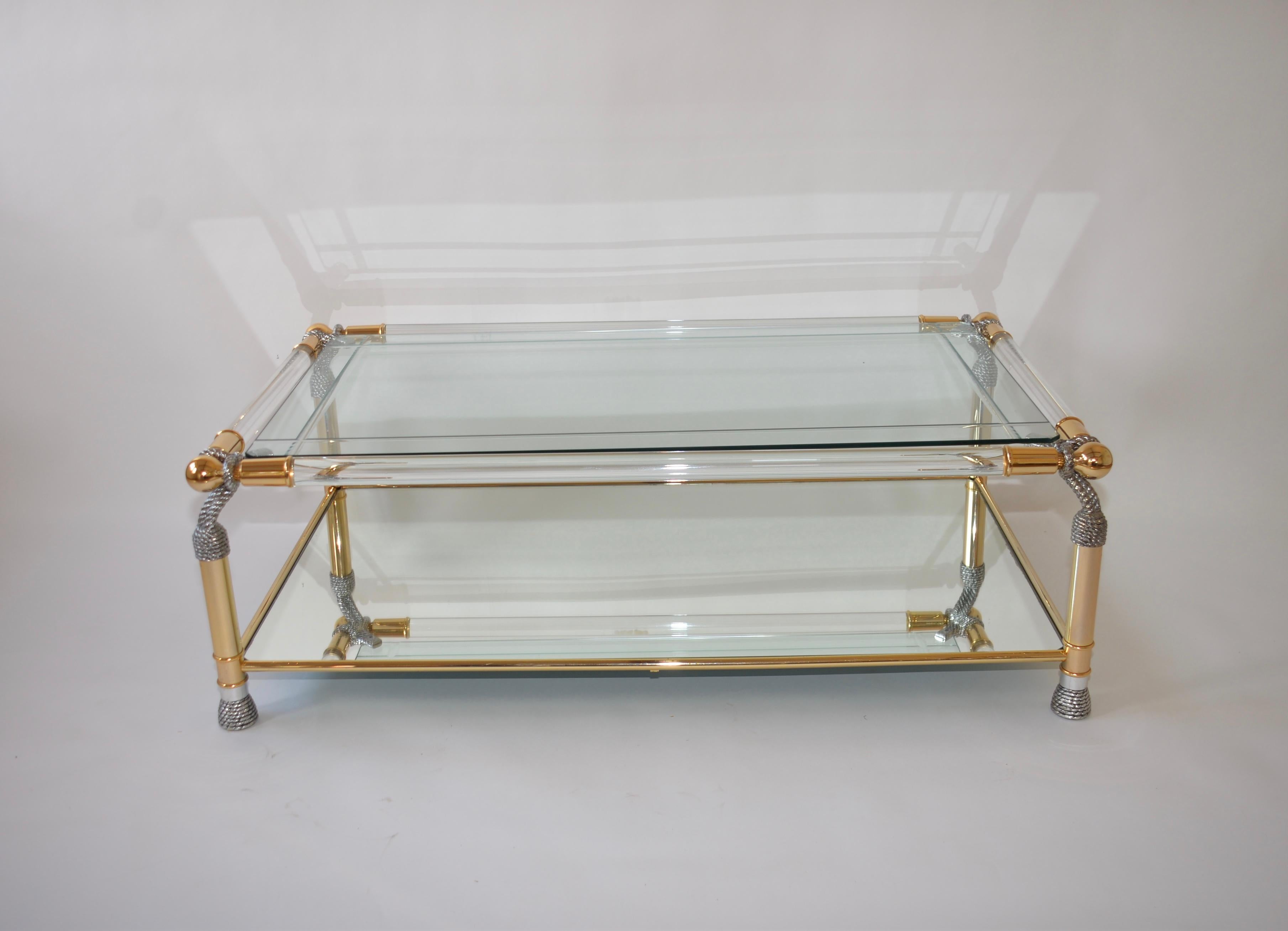 A striking Lucite, polished glass and beveled glass Hollywood Regency style coffee table. Two tiers, the top shelf is of beveled glass with the lower shelf being mirrored glass. Each corner has a twisted rope effect making this a very glamorous item.