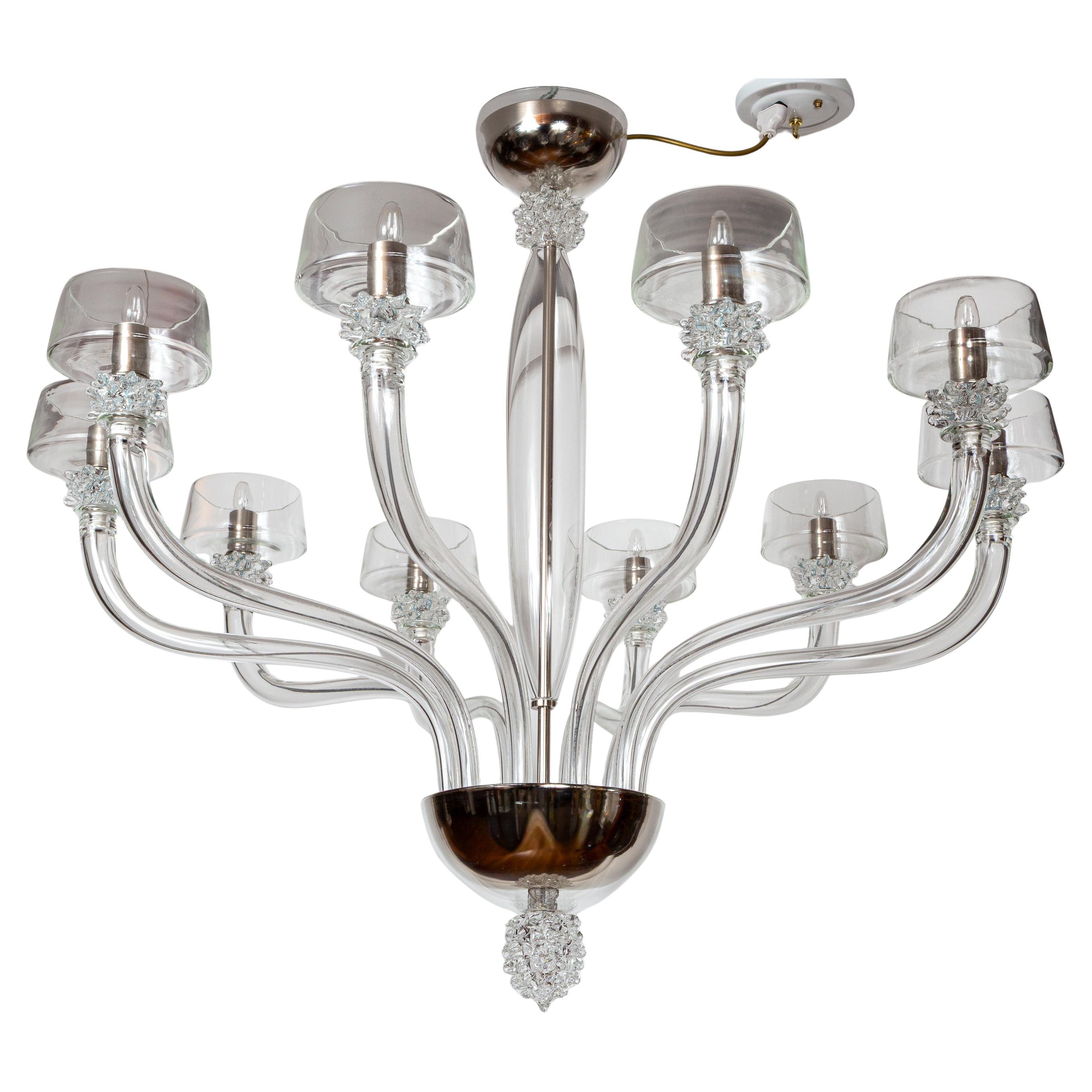 Lustre moderne et élégant en verre transparent soufflé à la bouche, composé de dix bras se terminant par des ferrures en rostrato soutenant des bobèches à angles profonds dans lesquelles la lumière de la lampe à incandescence se fait entendre.  les