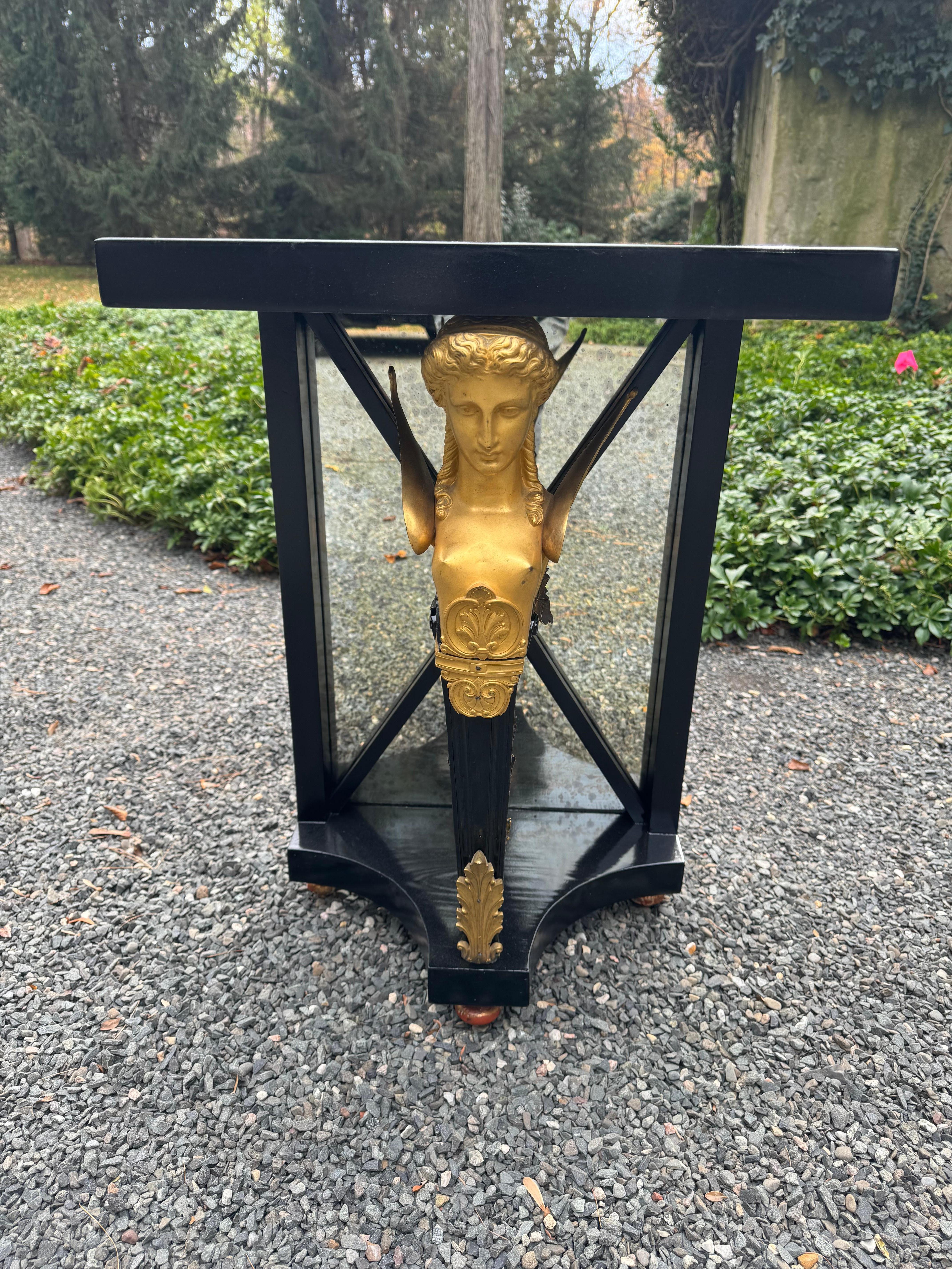 Stunning ebonized and gilt carytid side table in the neoclassical style having black laquered wood and gilt metal mounts with dramatic central figural form.  Table is backed with antique mirror. 