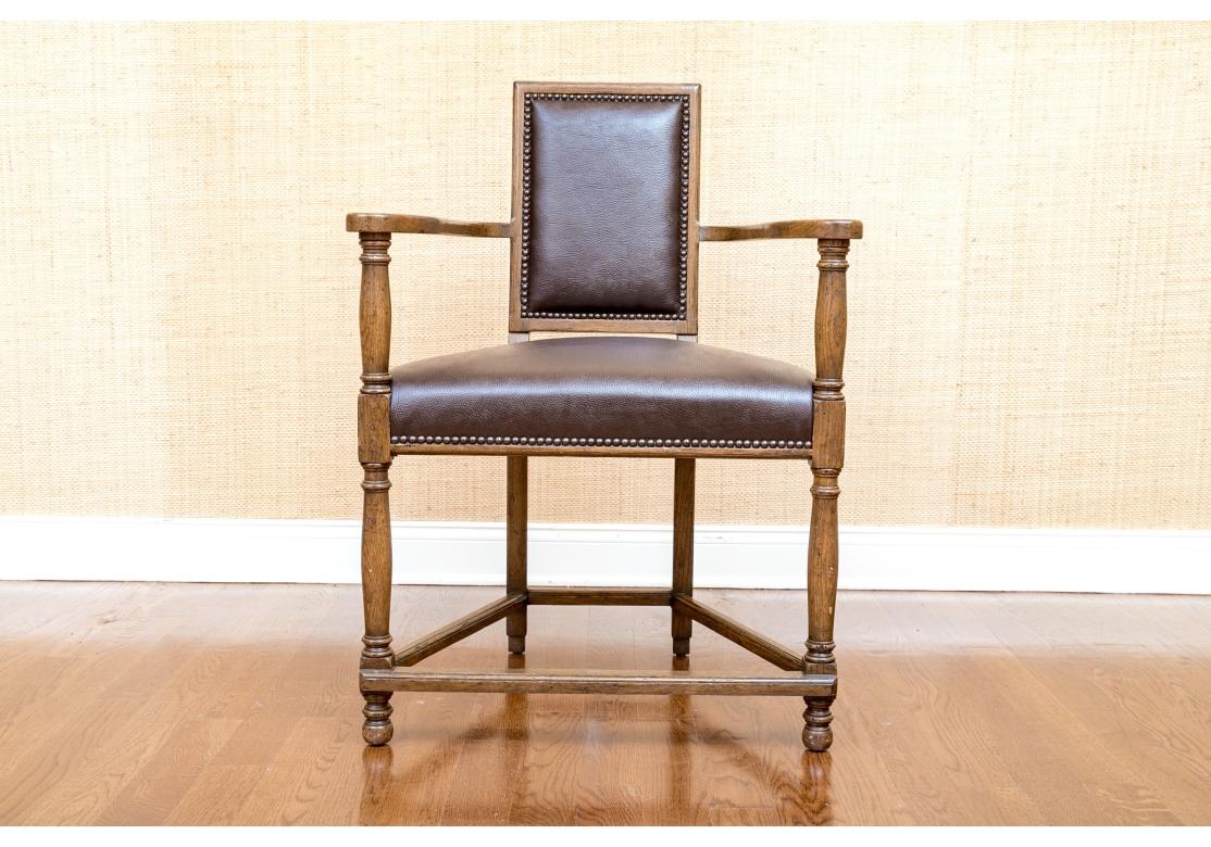A notable Oak Frame English Style Armchair with handsome faux or possibly real deep brown leather seat and back, both with brass nail-head decorative trim. With an unusual and highly decorative almost triangular form and having curved flat panel