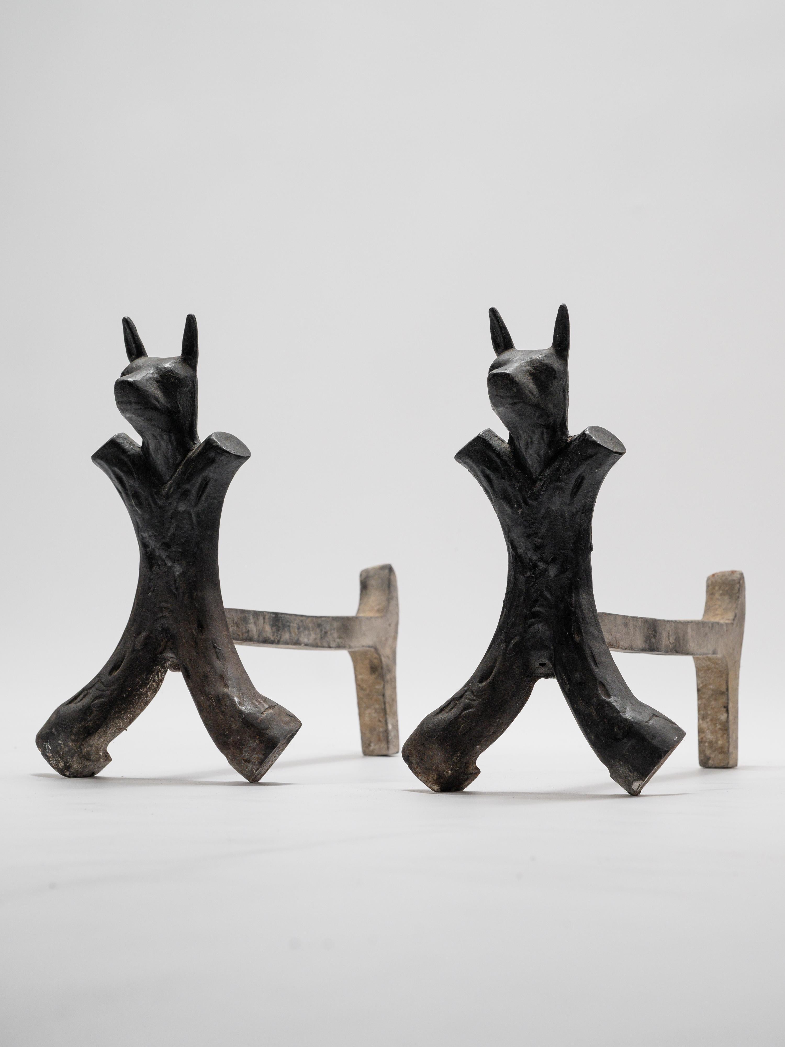 This striking pair of French wrought iron andirons from the 1950s embodies both functionality and sculptural presence. Crafted with solid forged iron, they feature stylized dog heads, their pointed ears and elongated snouts lending a protective and